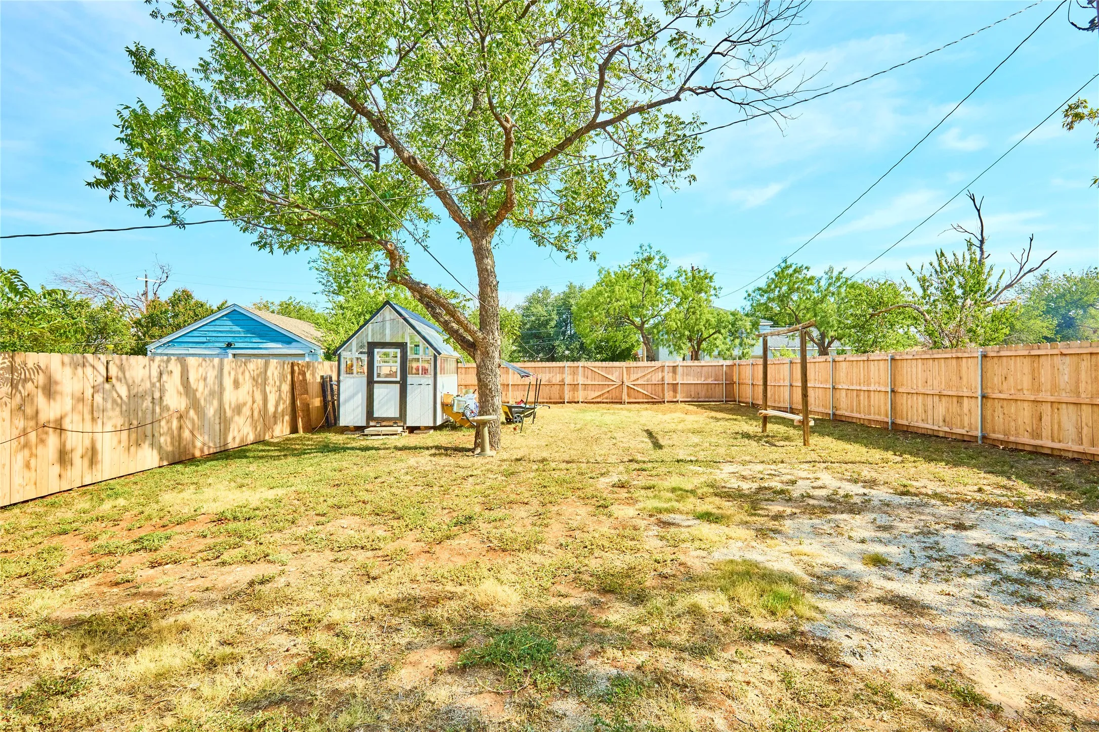 Expansive fenced backyard featuring a detached shed, a mature tree, and a wooden swing structure