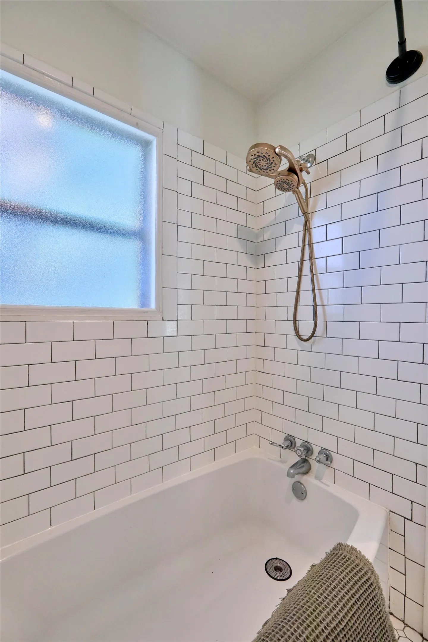White subway tile shower surround with a fixed showerhead and handheld sprayer, featuring a built-in tub