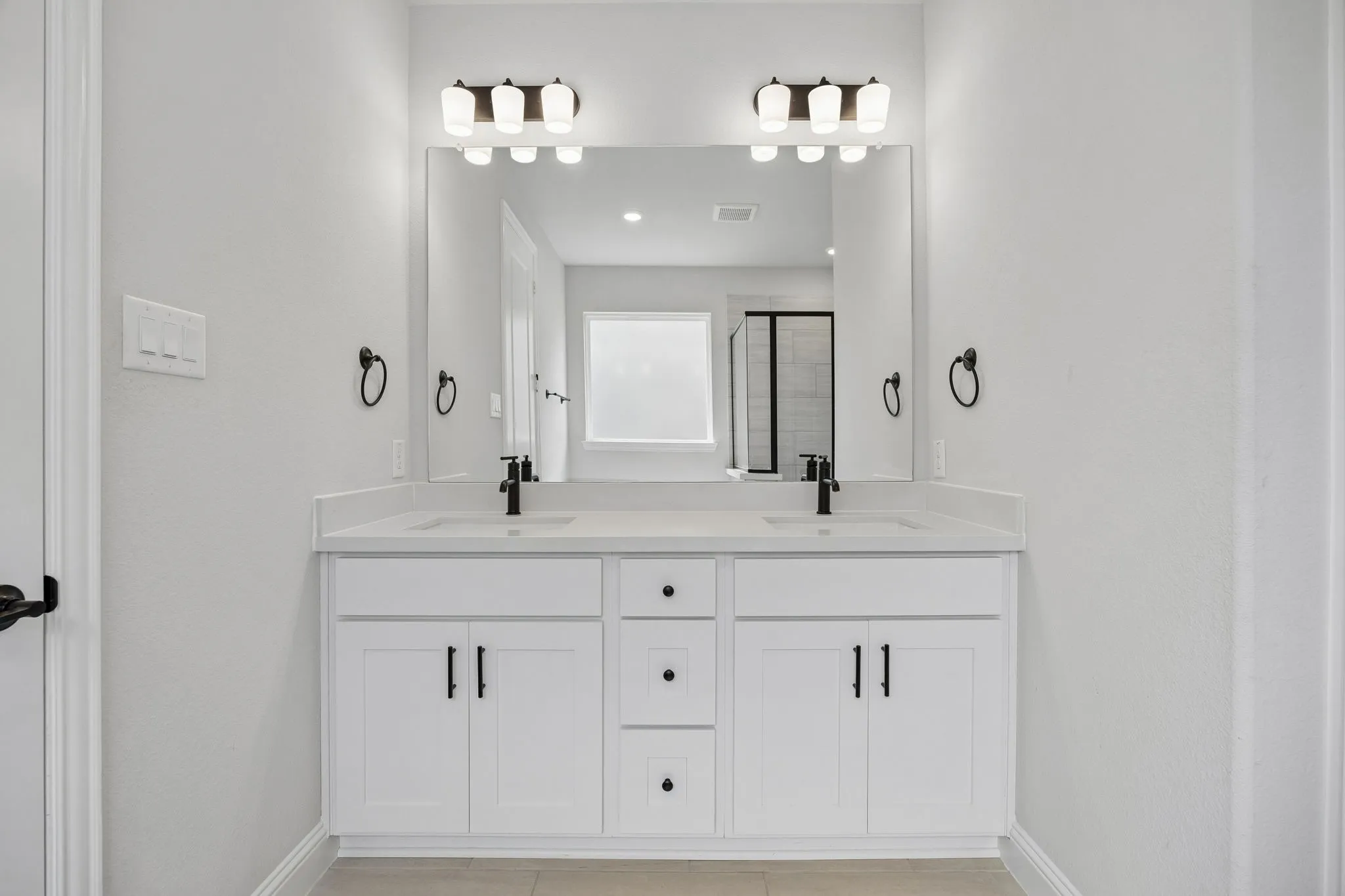 White double vanity with integrated sinks, black fixtures, and a large mirror