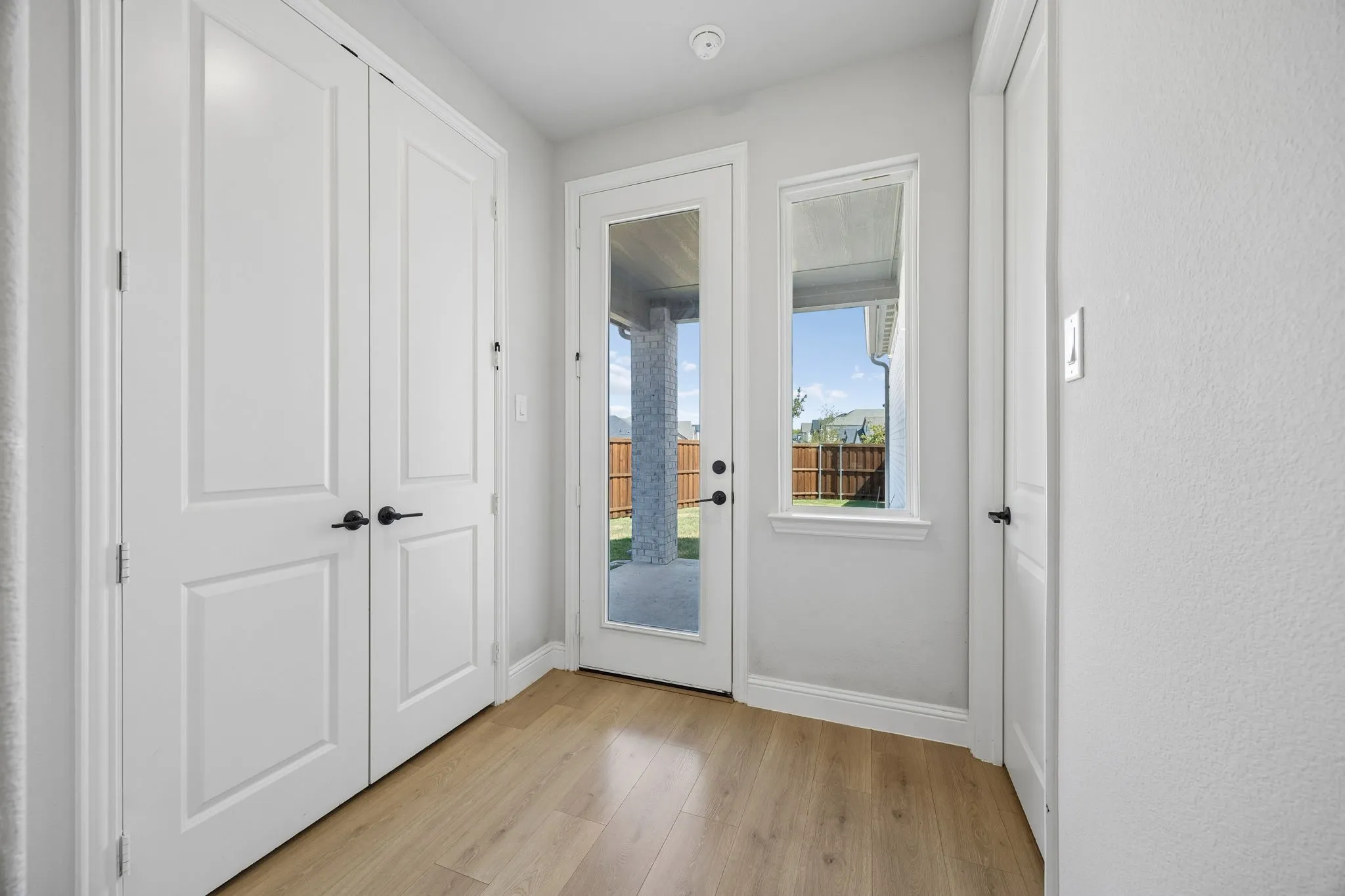Wood-finish flooring, white paneled doors with black hardware, full-light glass door, and a transom window