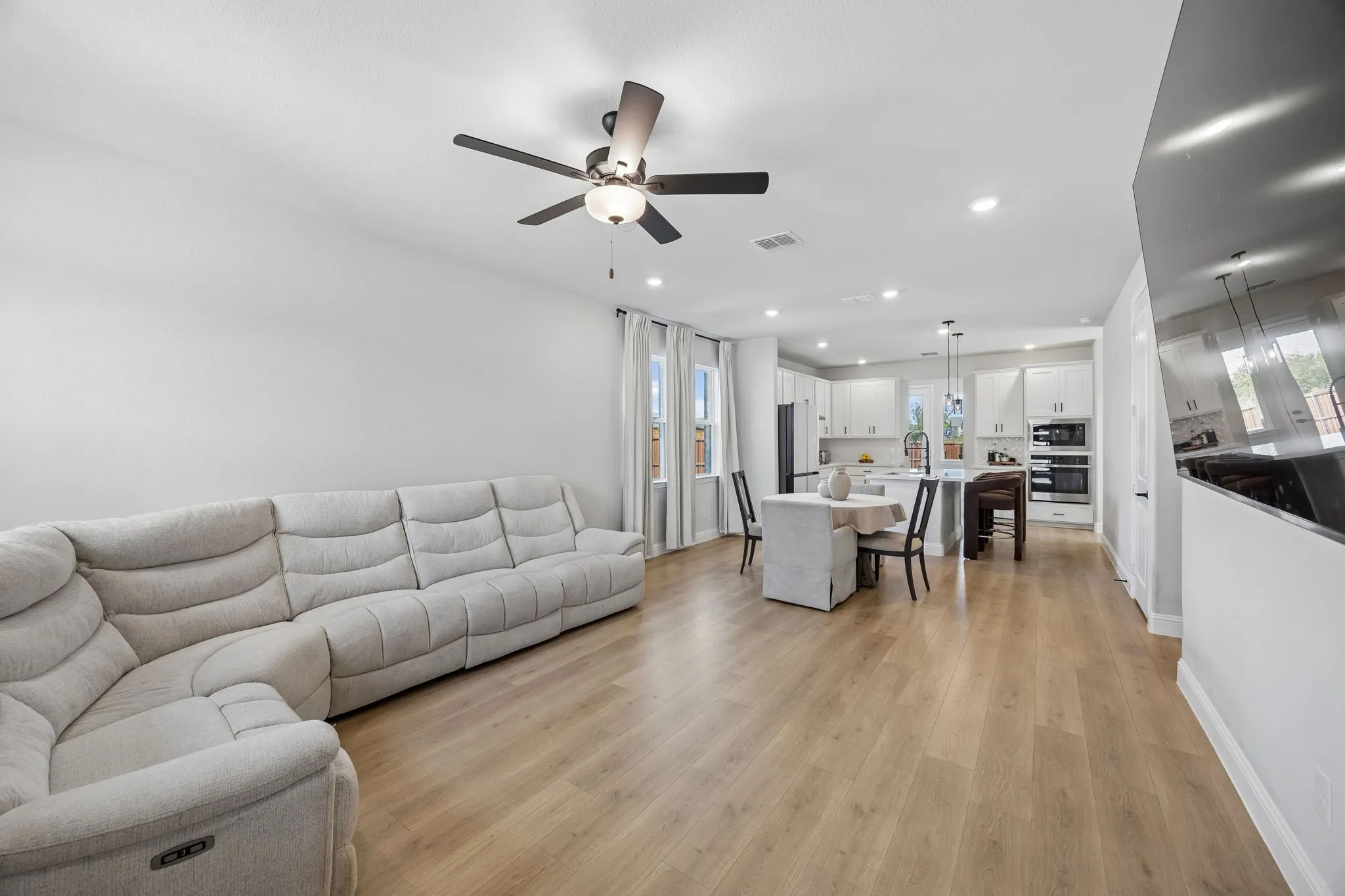 Open-concept living space featuring wood-finish flooring, recessed lighting, a ceiling fan, and white painted walls