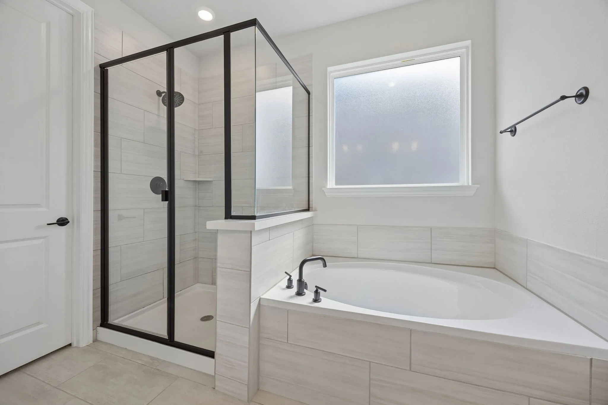 Corner soaking tub with a tiled surround, adjacent to a shower with a black-framed glass enclosure