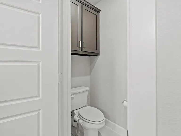 White paneled door with a privacy lock, wall-mounted cabinetry, and a commode