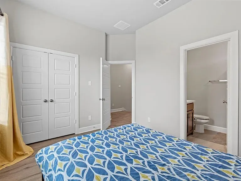 Vaulted ceiling, two-panel closet doors, wood-finish flooring, white walls, and a private bath with a vanity and toilet