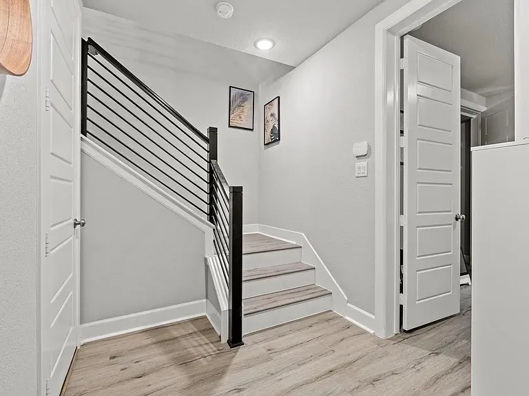 Wood-finish flooring, staircase with horizontal black metal railing, recessed lighting, and white paneled doors