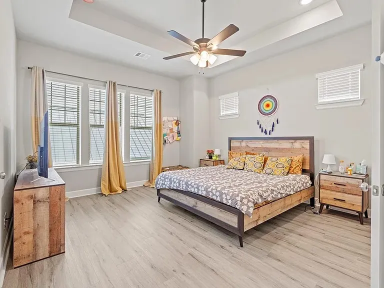 Tray ceiling with recessed lighting and a ceiling fan, light wood-finish flooring, and multiple windows with blinds