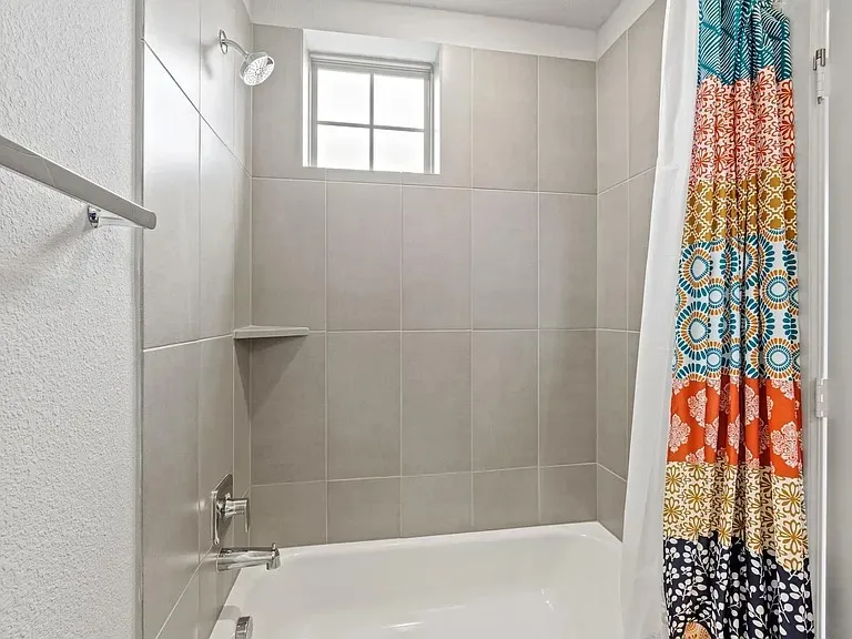 Bathtub and shower combination featuring light gray subway tile surround, built-in shelving, a chrome showerhead, and a chrome faucet