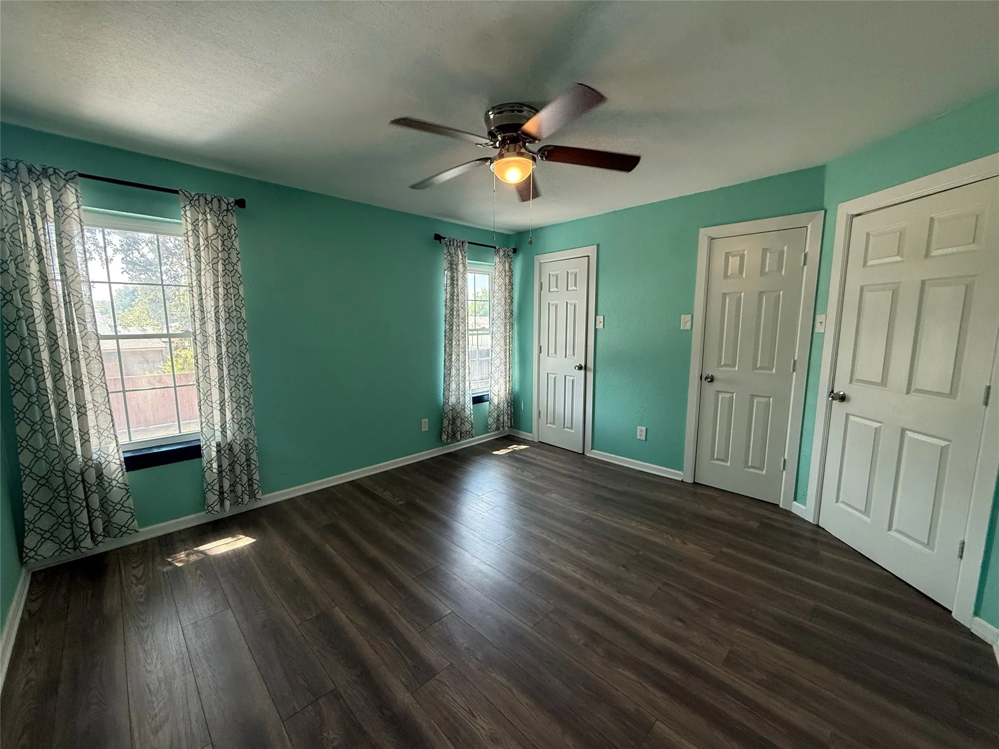Wood-finish flooring, two windows, three paneled doors, and a ceiling fan with integrated lighting