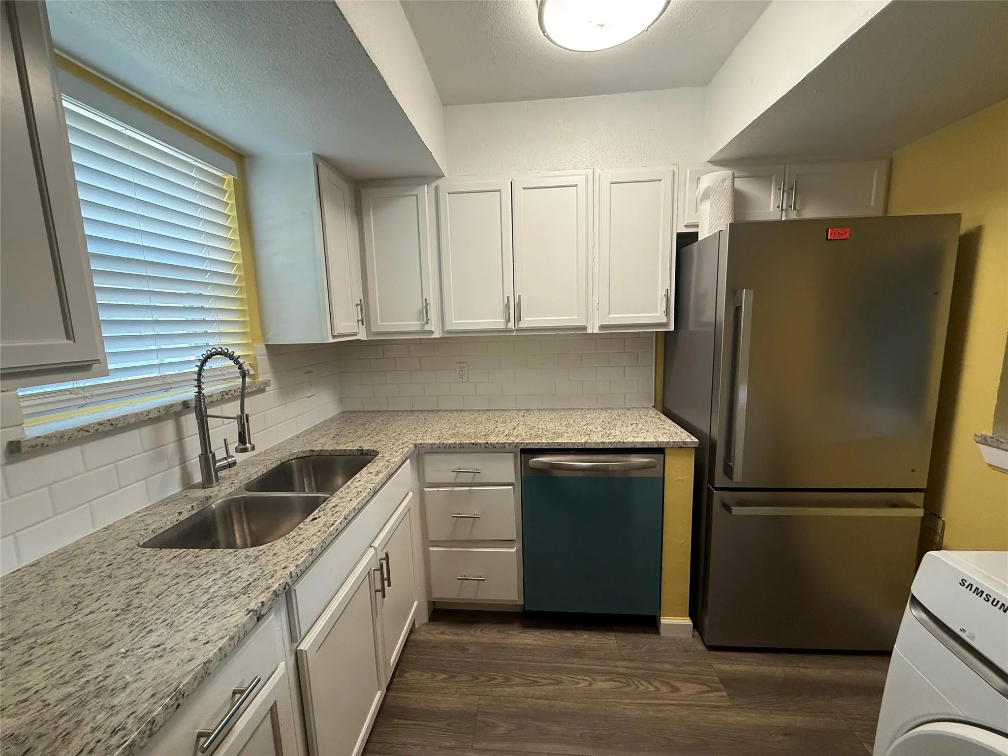 Kitchen featuring light-toned cabinetry, granite-finish countertops, subway tile backsplash, and stainless steel appliances
