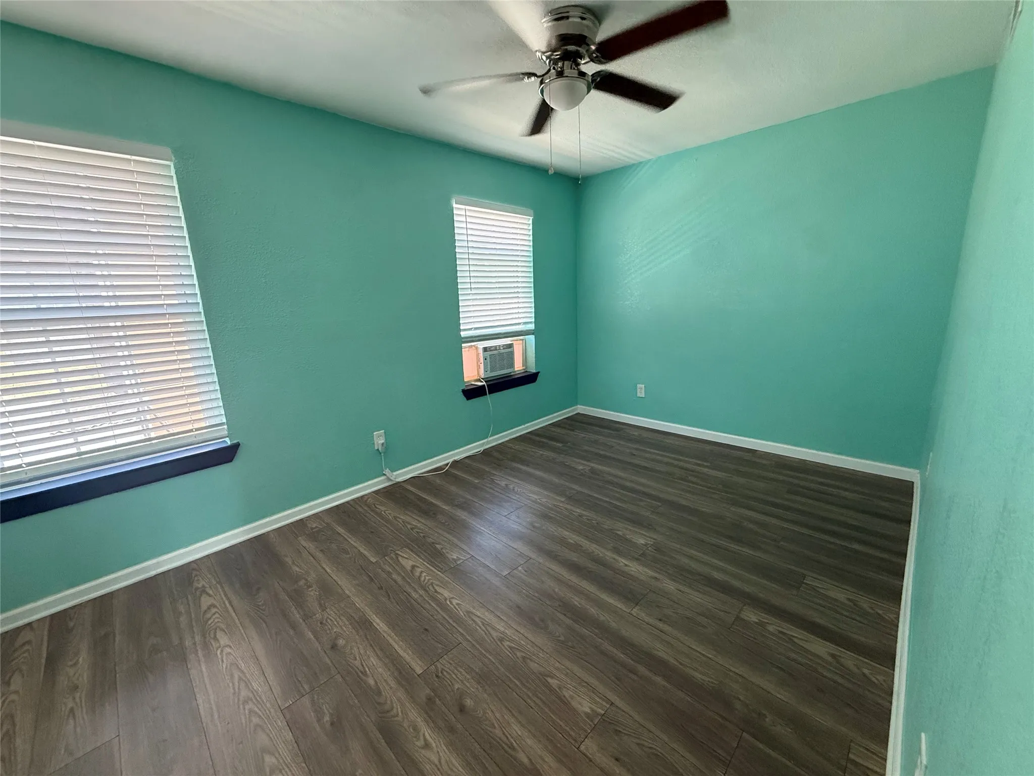 Wood-finish flooring, ceiling fan, and two windows with blinds
