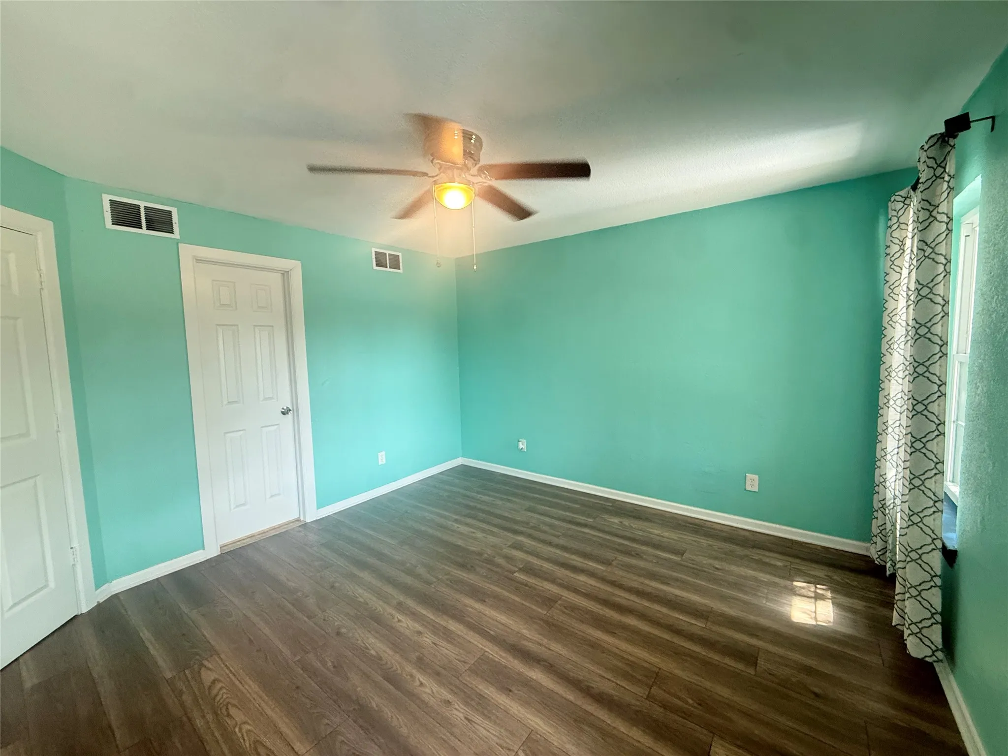 Wood-finish flooring, ceiling fan with integrated lighting, white interior doors, and a window for natural light