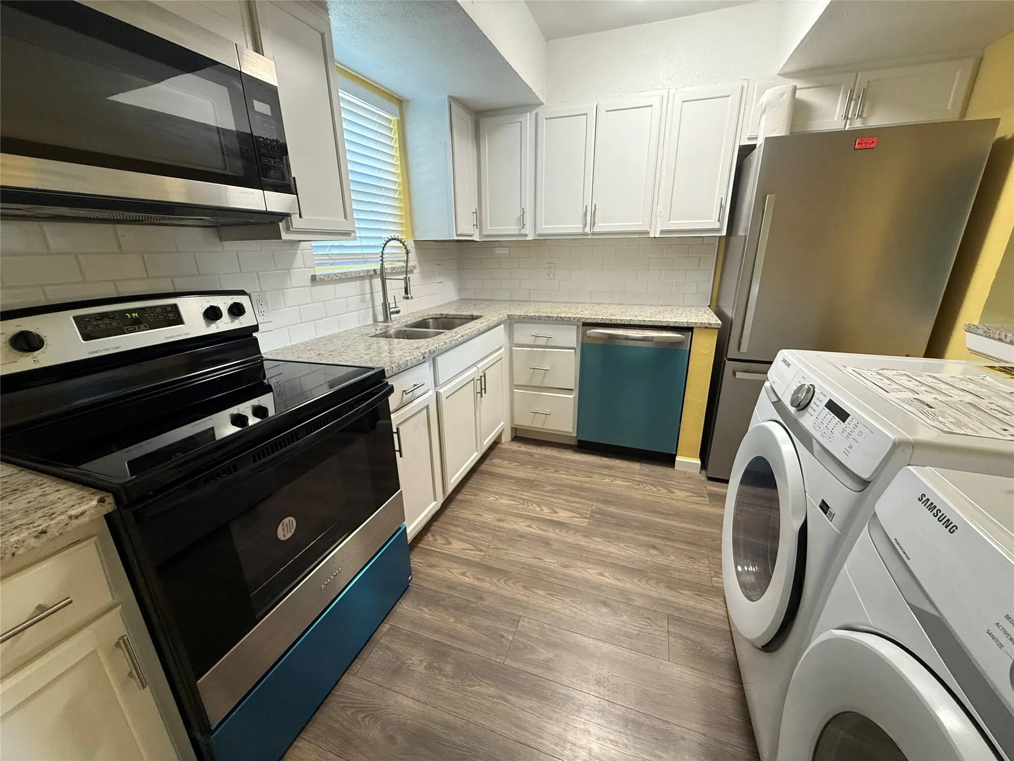 Kitchen featuring wood-finish flooring, white cabinetry, granite countertops, and a subway tile backsplash