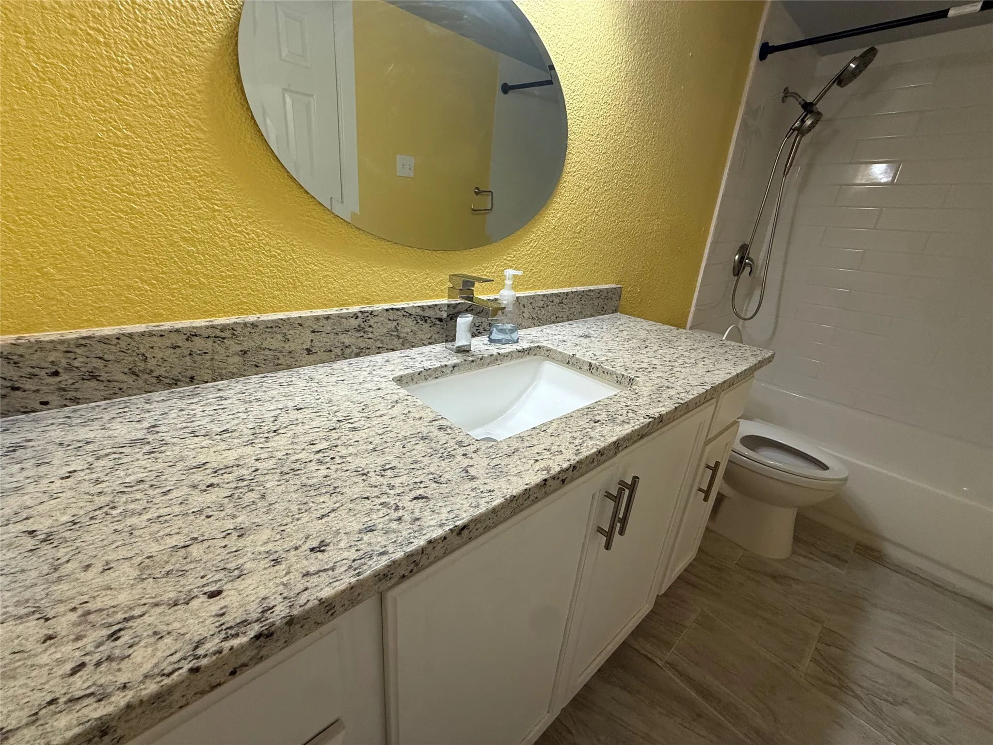Vanity with a speckled countertop, integrated sink, and white cabinetry featuring bar pulls