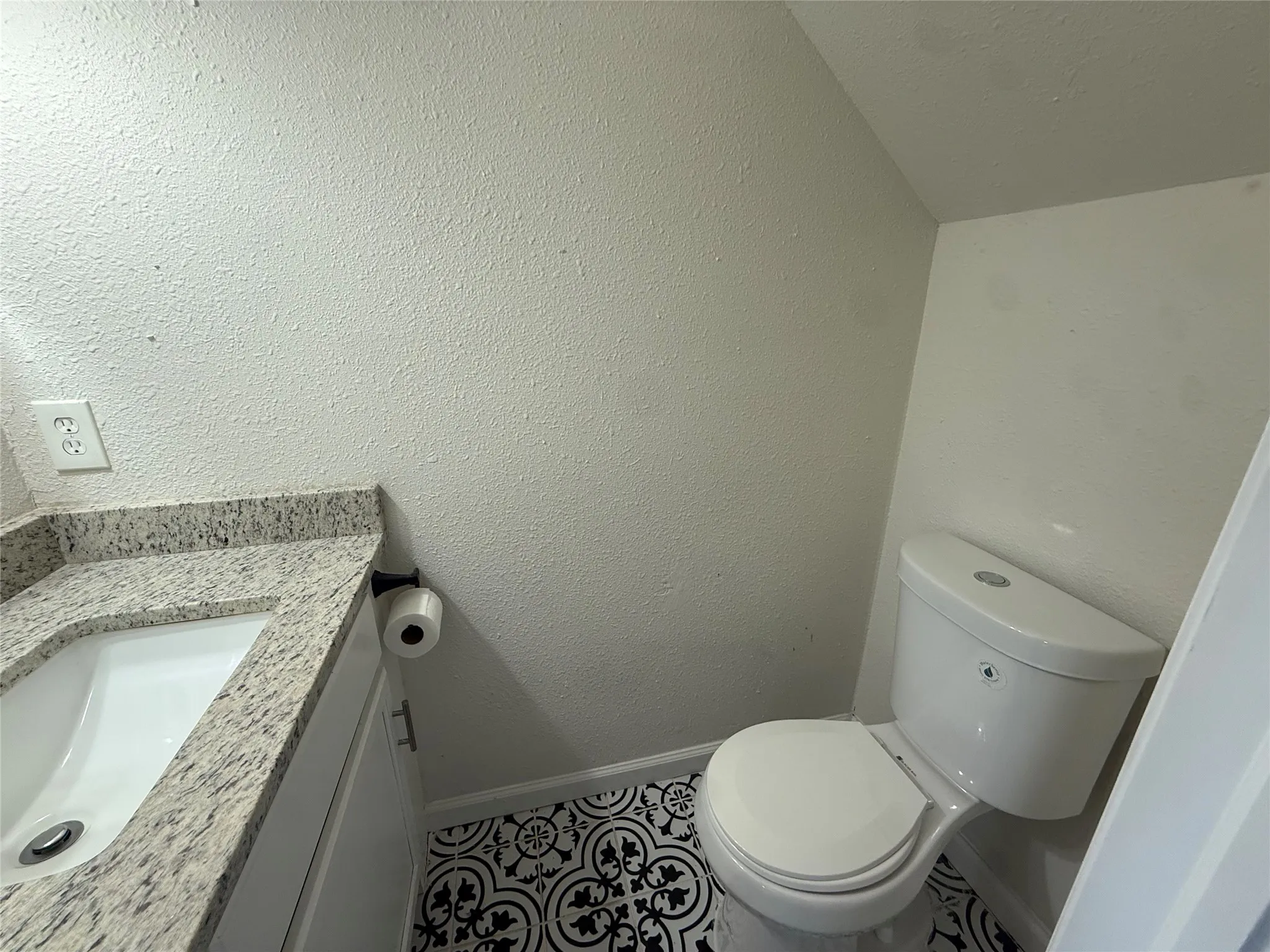 Vanity with an undermount sink and a speckled countertop, toilet, and patterned flooring