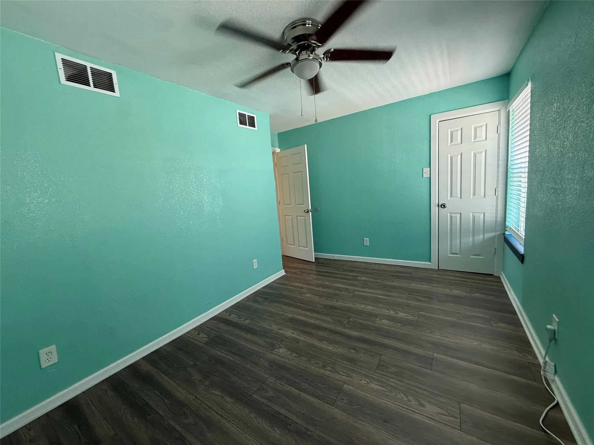 Wood-finish flooring with white baseboards, a ceiling fan with light fixture, and white paneled interior doors
