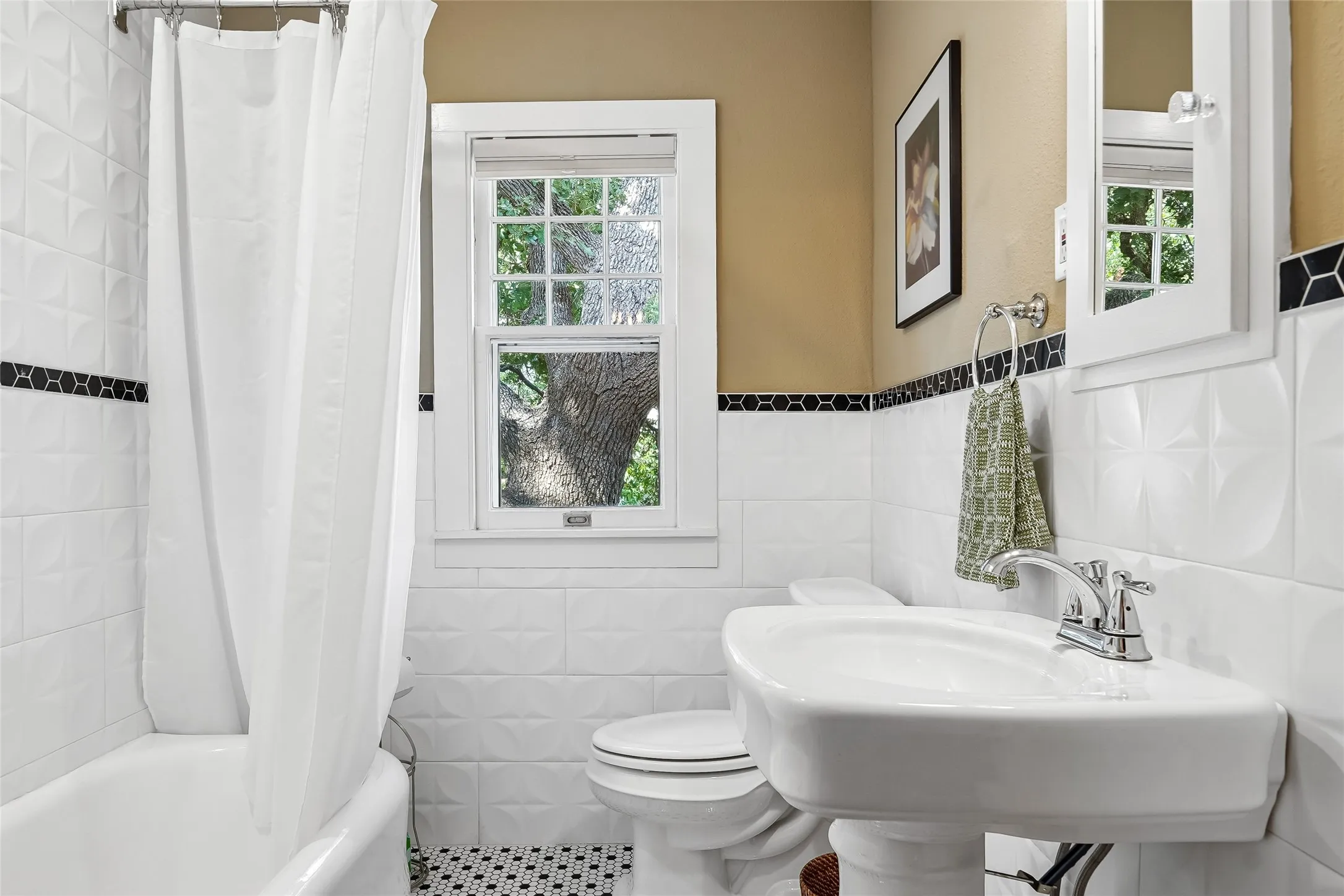 Pedestal sink with chrome faucet, white tiled walls with decorative black accent band, patterned black and white floor tiles, and a window providing natural light