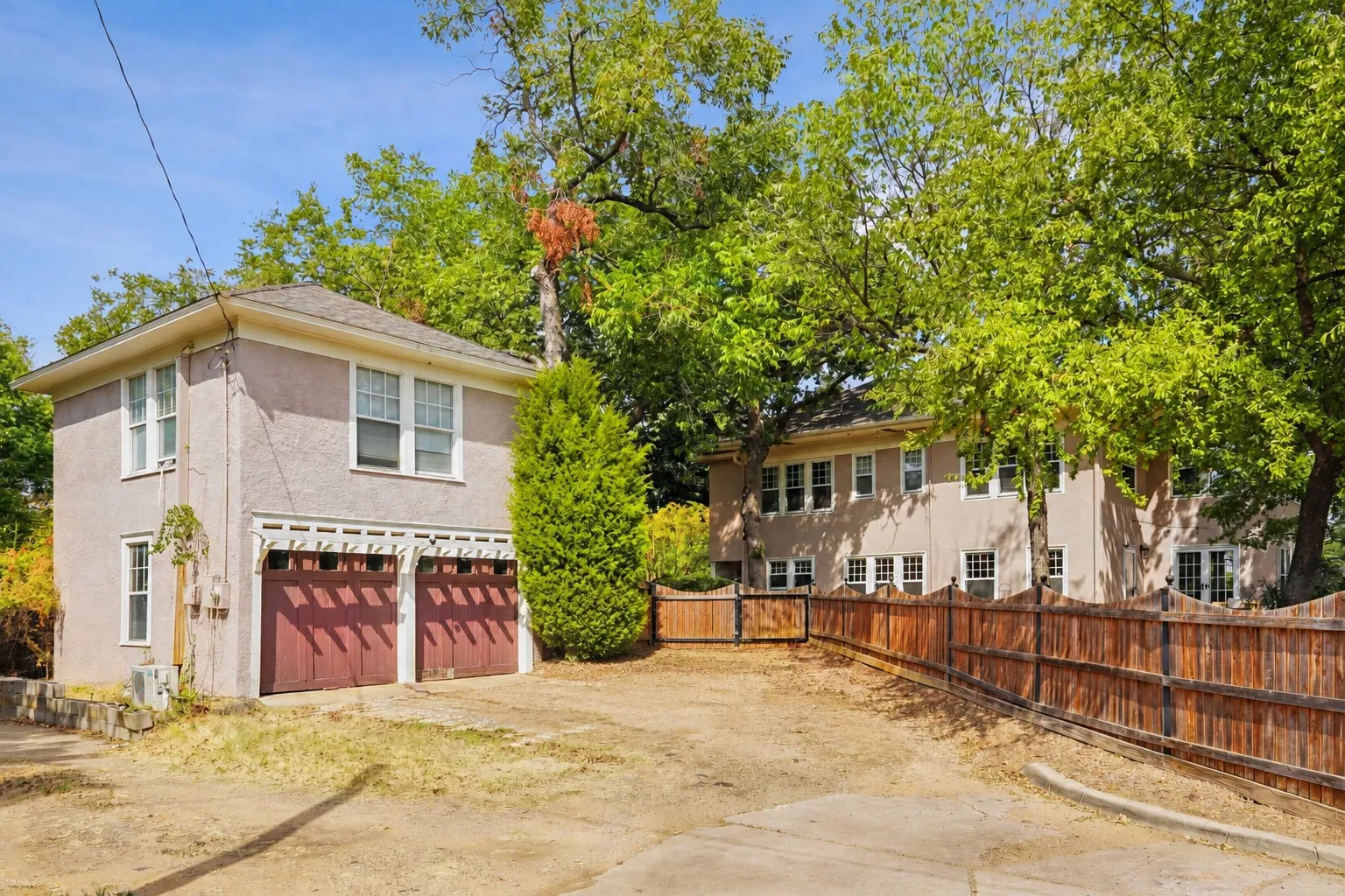 Two-story stucco building with dual garage doors, surrounded by established trees