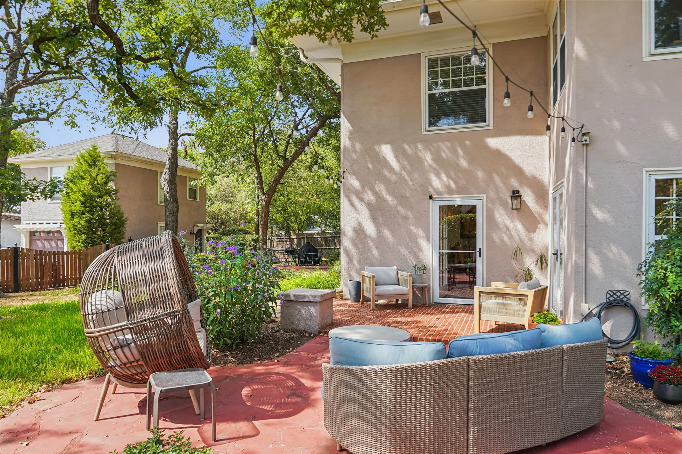 Stucco exterior with multiple windows, red paver patio, and mature trees