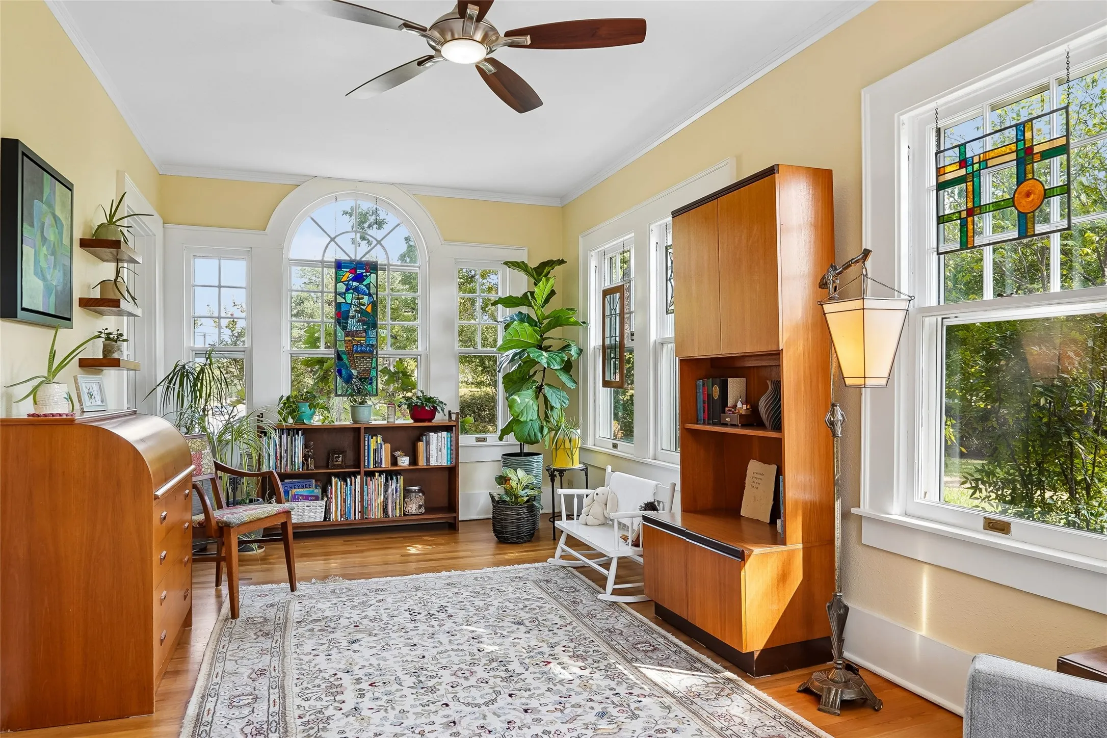 Hardwood flooring, arched window with stained glass, ceiling fan with integrated lighting, built-in shelving, multiple windows