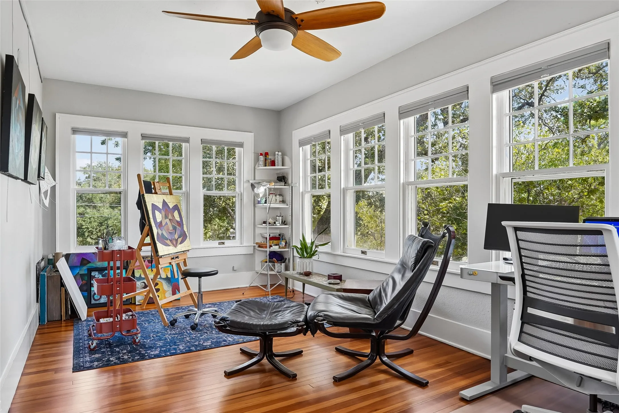 Hardwood flooring, multiple grid-pattern windows, paneled walls, ceiling fan, and white trim throughout