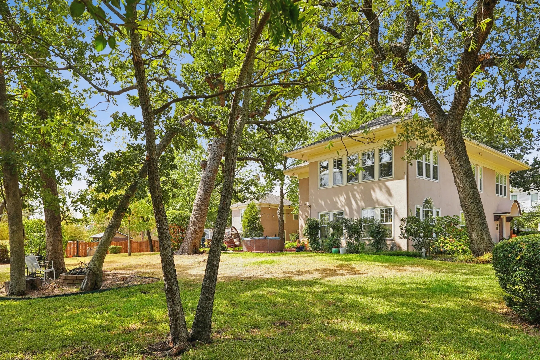 Stucco exterior with multiple windows, mature trees, and a manicured lawn