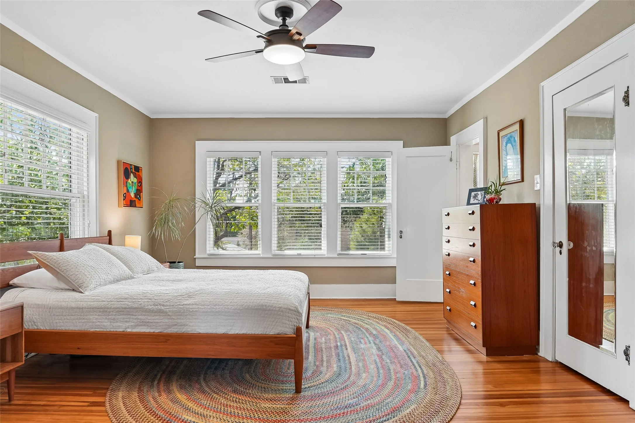 Wood-finish flooring, crown molding, ceiling fan with integrated lighting, and multiple windows with blinds