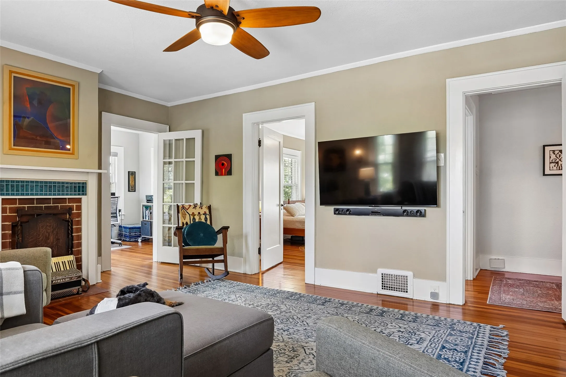 Hardwood flooring, painted trim, brick fireplace with tile surround, ceiling fan, and French doors