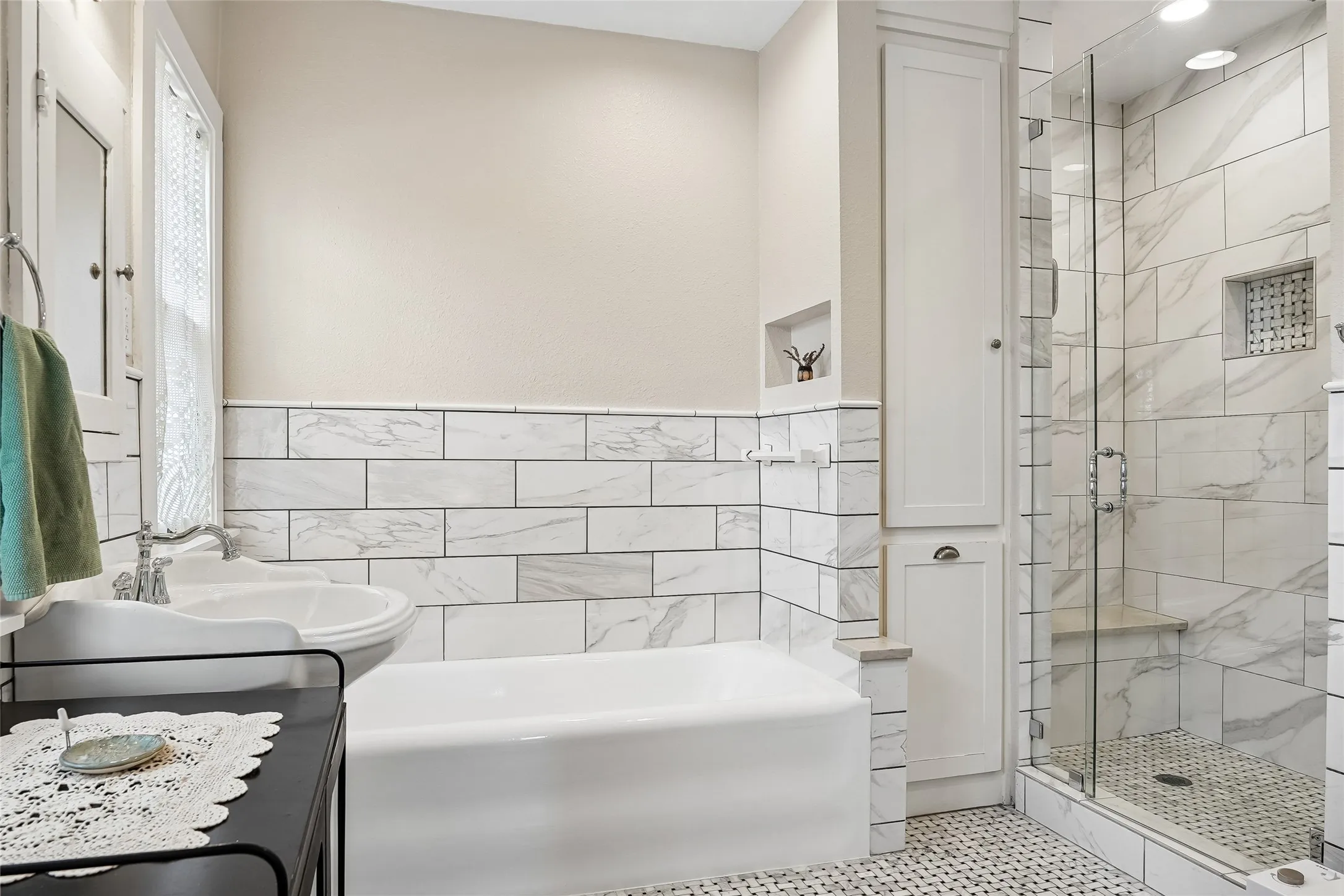 Bathroom featuring a built-in tub, separate glass-enclosed shower with bench, tiled walls, built-in cabinetry, and a pedestal sink