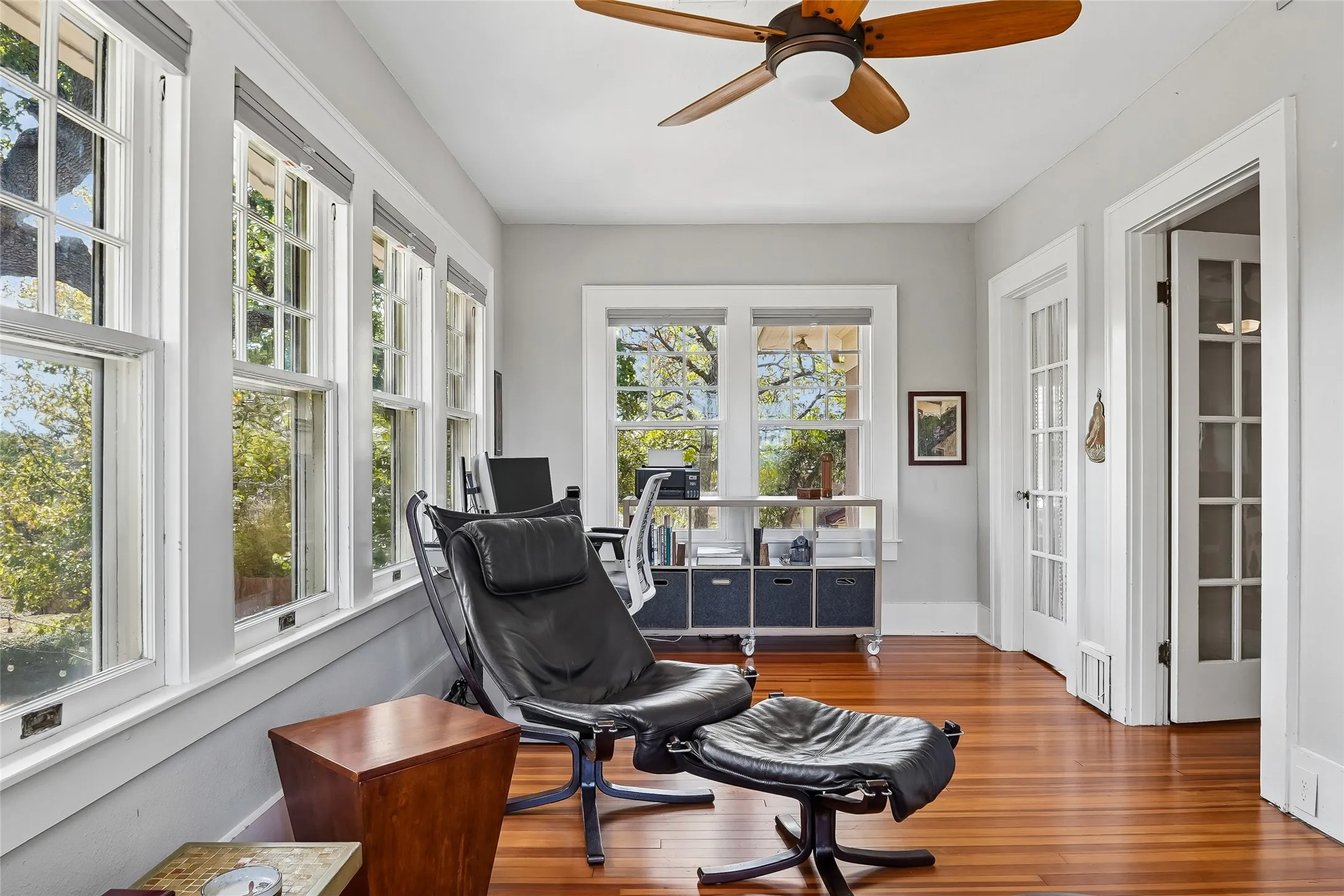Hardwood flooring, multiple windows with white trim, white paneled French doors, and a ceiling fan with integrated lighting