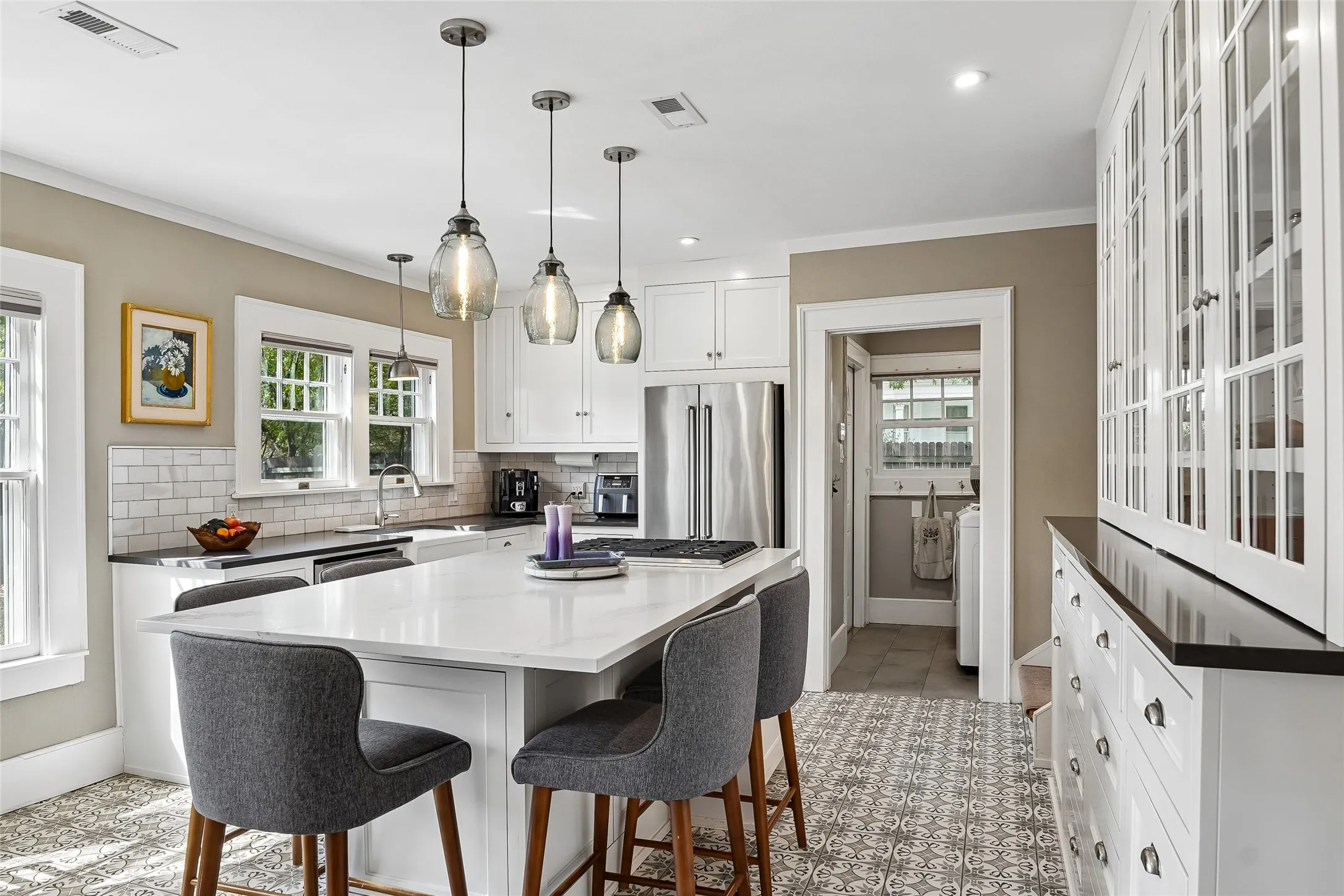 White cabinetry, stainless steel appliances, white subway tile backsplash, patterned floor tile, and a large central island with seating