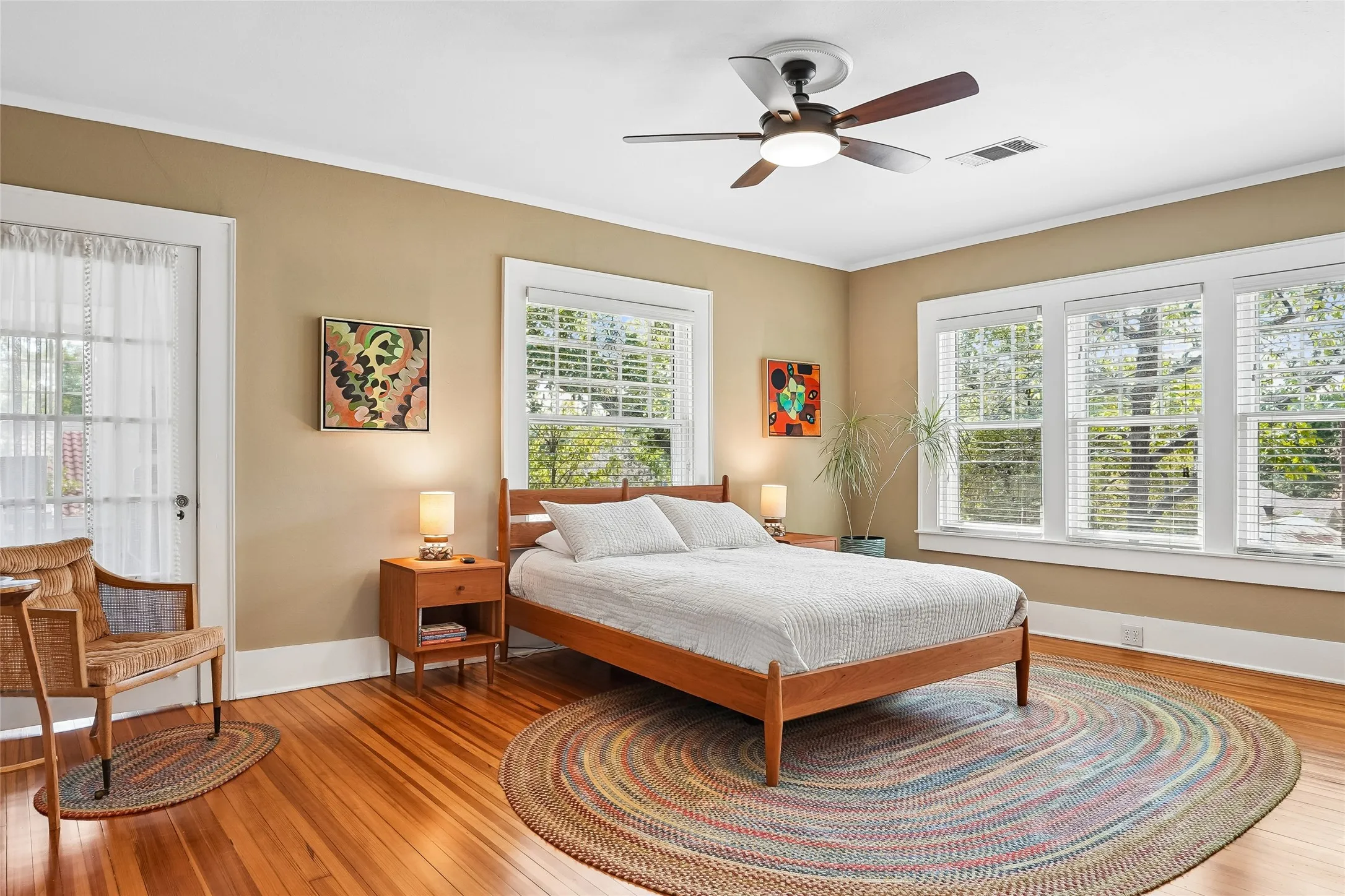 Wood-finish flooring, multiple windows with blinds, a ceiling fan with integrated lighting, and a white paneled door