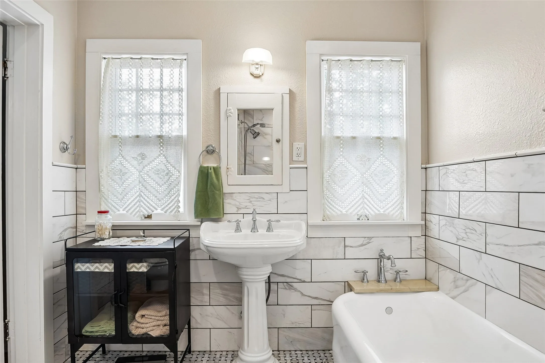 Pedestal sink, wall-mounted medicine cabinet, white subway tile surround, white bathtub, and patterned floor tile