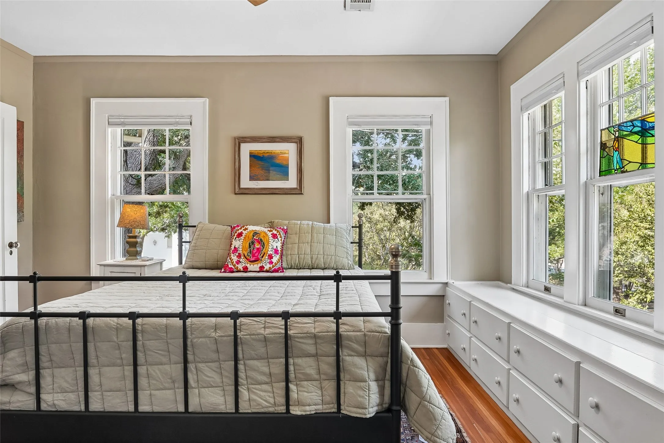 Hardwood flooring, multiple windows with white trim, built-in window seat with storage drawers, and an additional window featuring stained glass