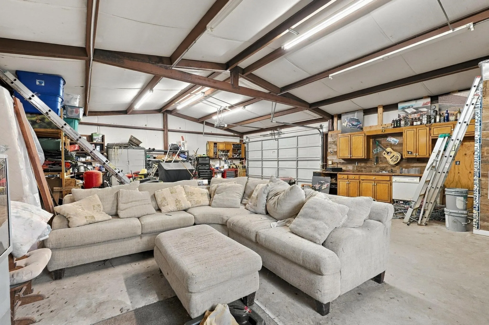 Spacious interior with exposed metal beams, concrete flooring, fluorescent lighting, and a roll-up garage door