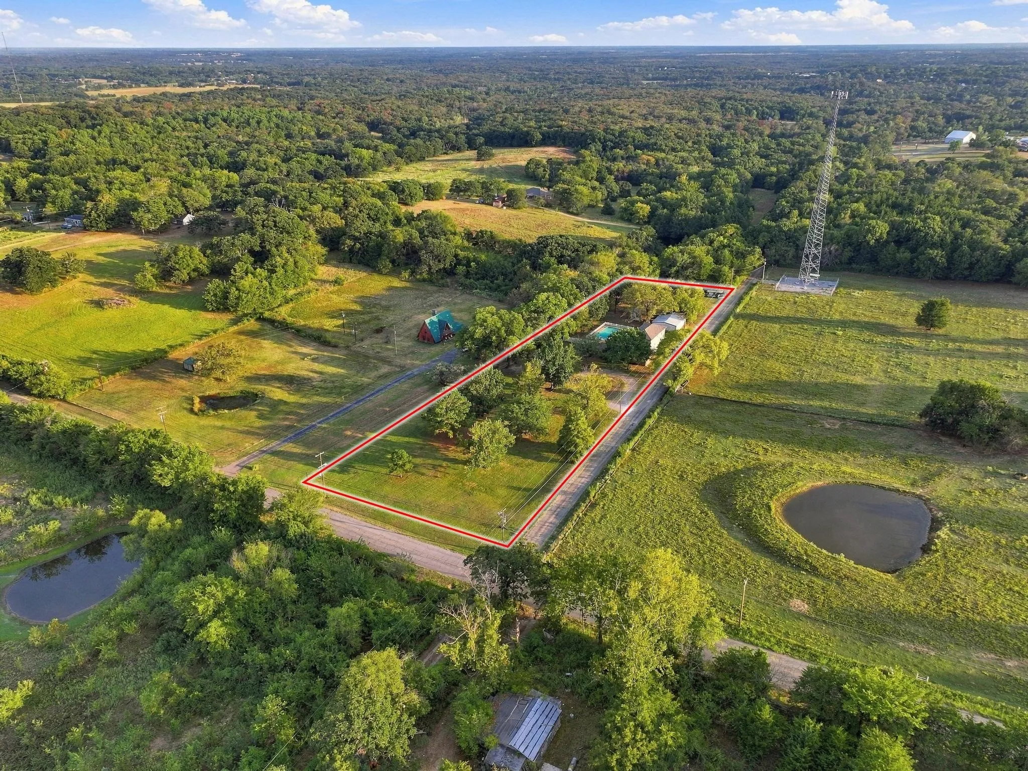 Expansive rural property featuring a primary residence, detached structure, swimming pool, and mature trees, surrounded by open fields