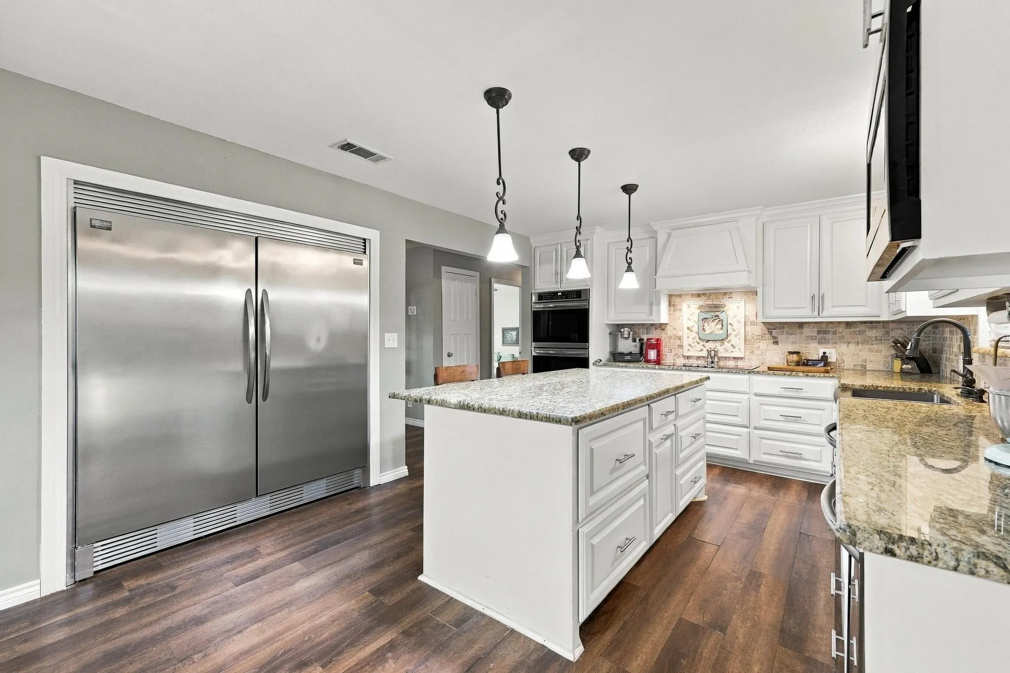 Kitchen featuring wood-finish flooring, a central island with granite countertop, white cabinetry with decorative hardware, and sub zero refrigerator