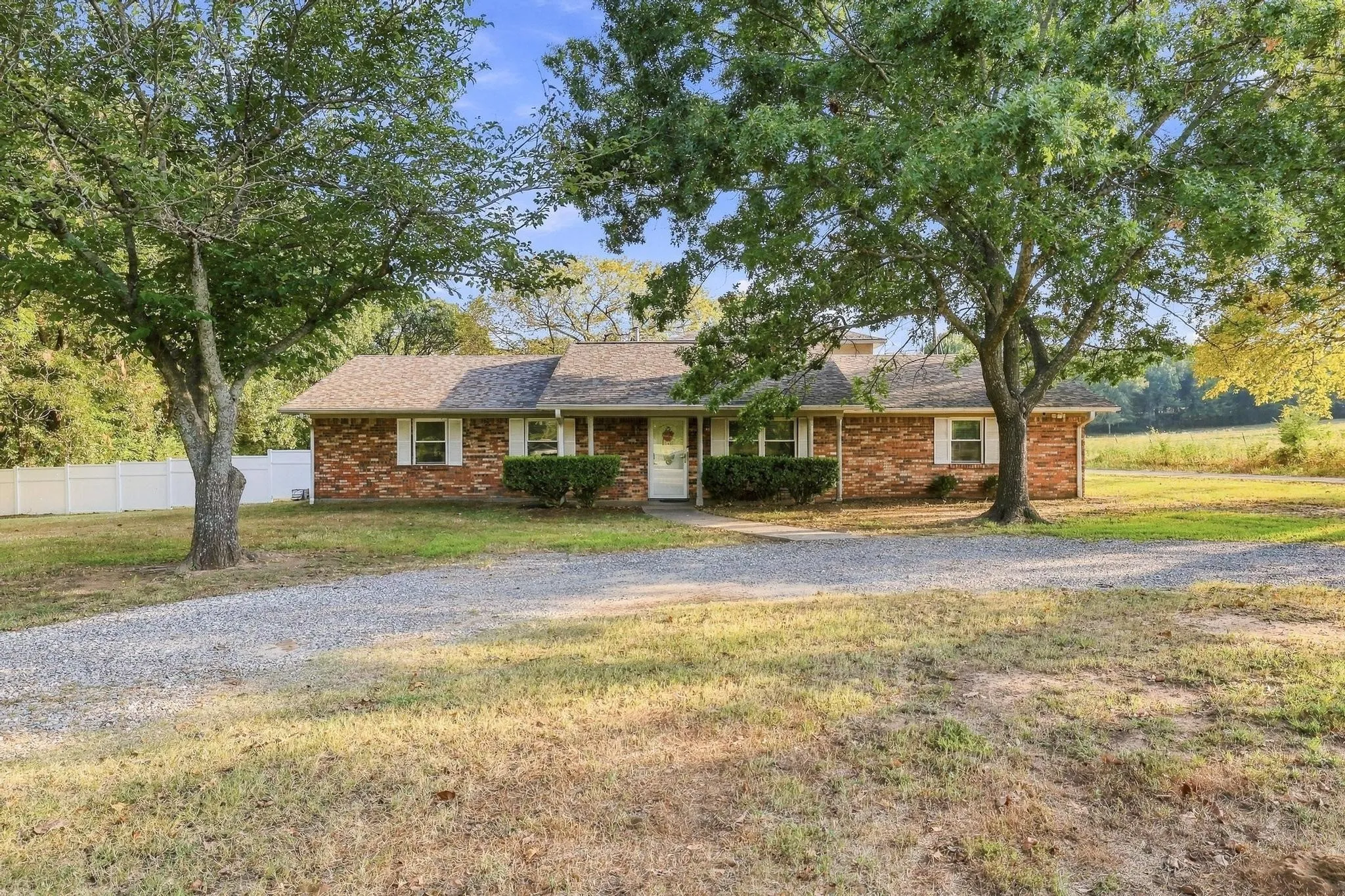 Brick exterior residence with a gravel driveway, mature trees