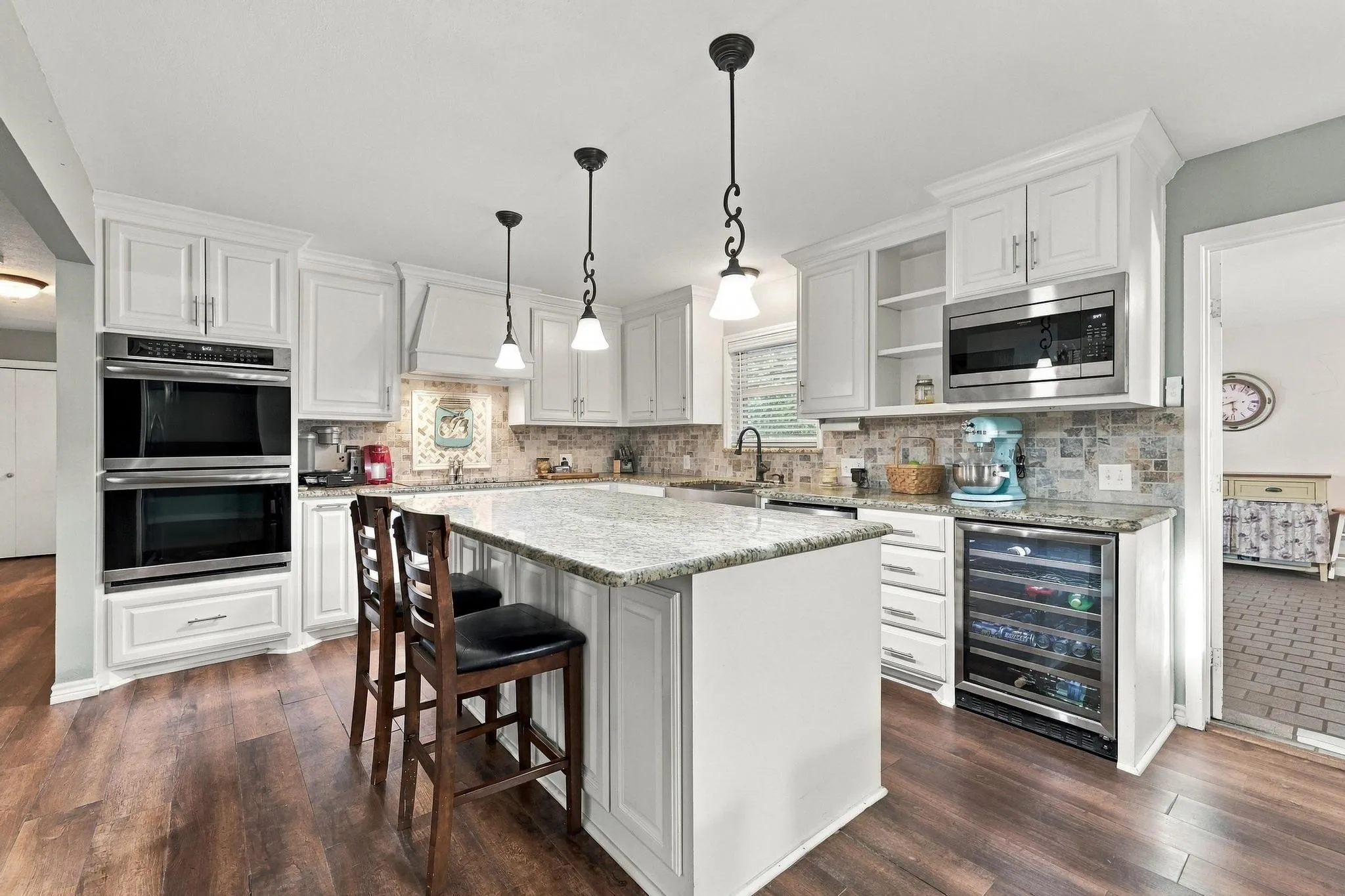 Kitchen featuring white cabinetry, wood-finish flooring, a central island with a light-toned countertop, built-in double ovens, and a beverage refrigerator