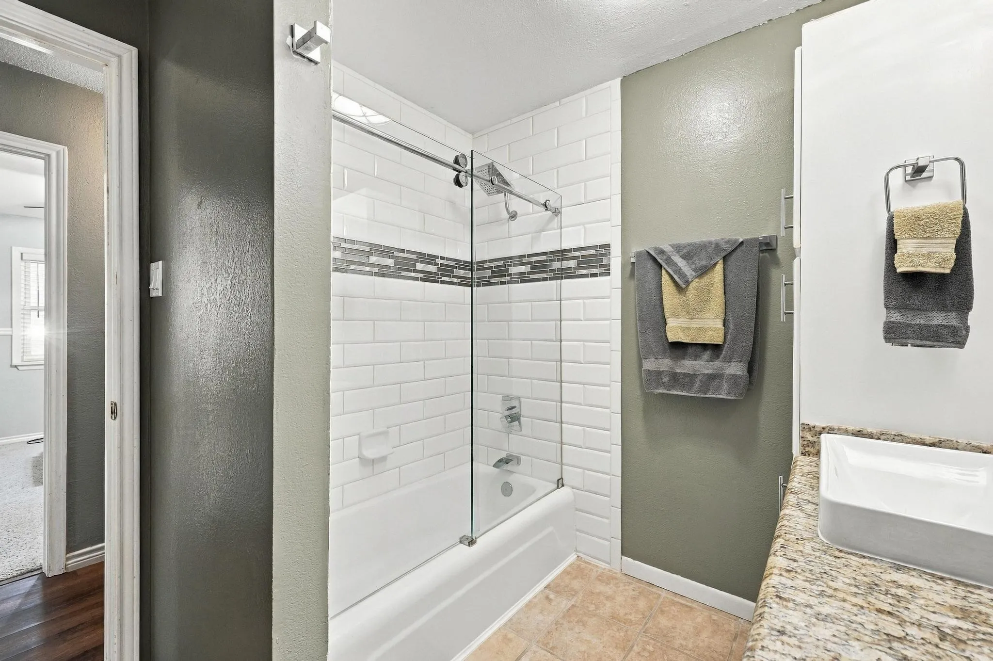 Bathtub with subway tile surround, glass sliding shower door, and decorative accent tile band