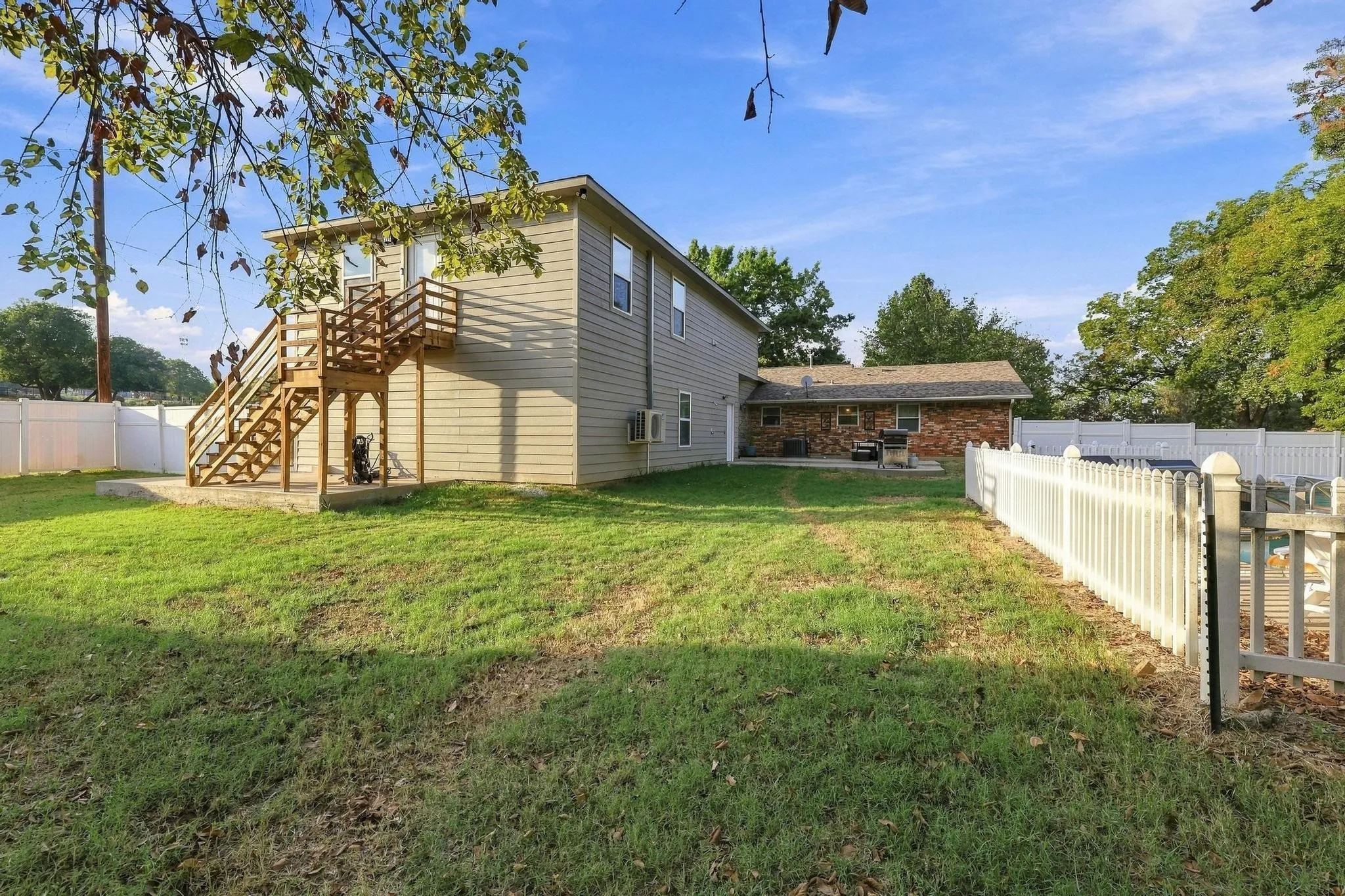 Expansive grassy yard with a white picket fence, a large deck with wood stairs, and a brick-faced structure