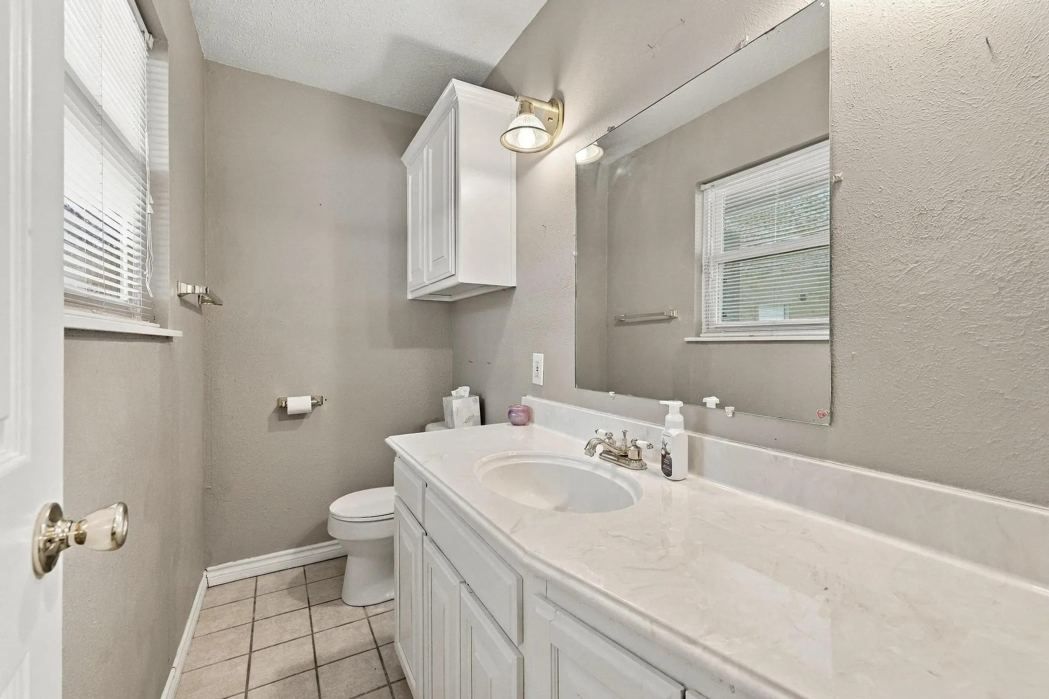 Vanity with integrated sink, white cabinetry, wall-mounted mirror, and tiled flooring