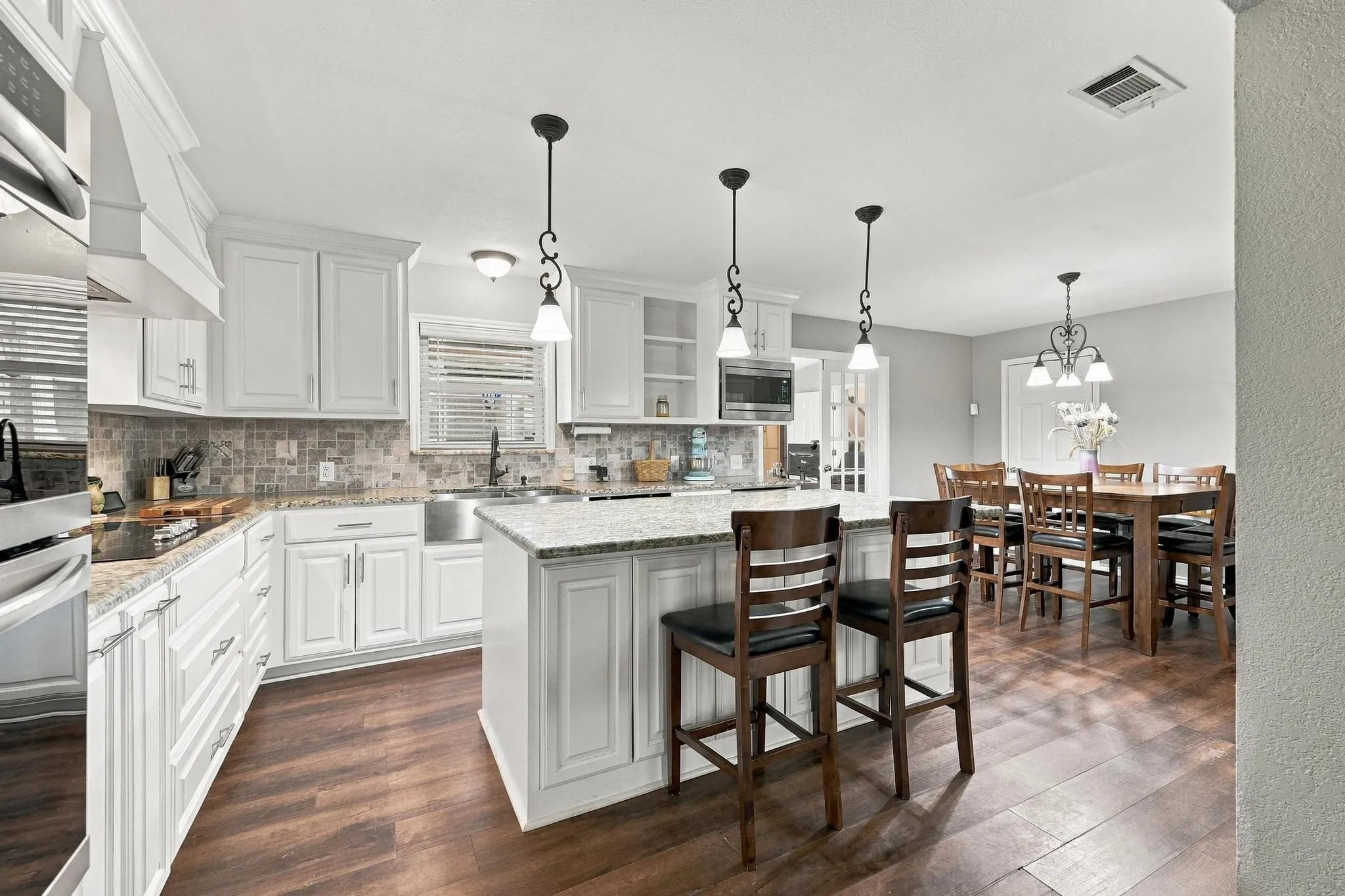 Kitchen featuring white cabinetry, granite countertops, stainless steel appliances, a center island with pendant lighting, and wood-finish flooring