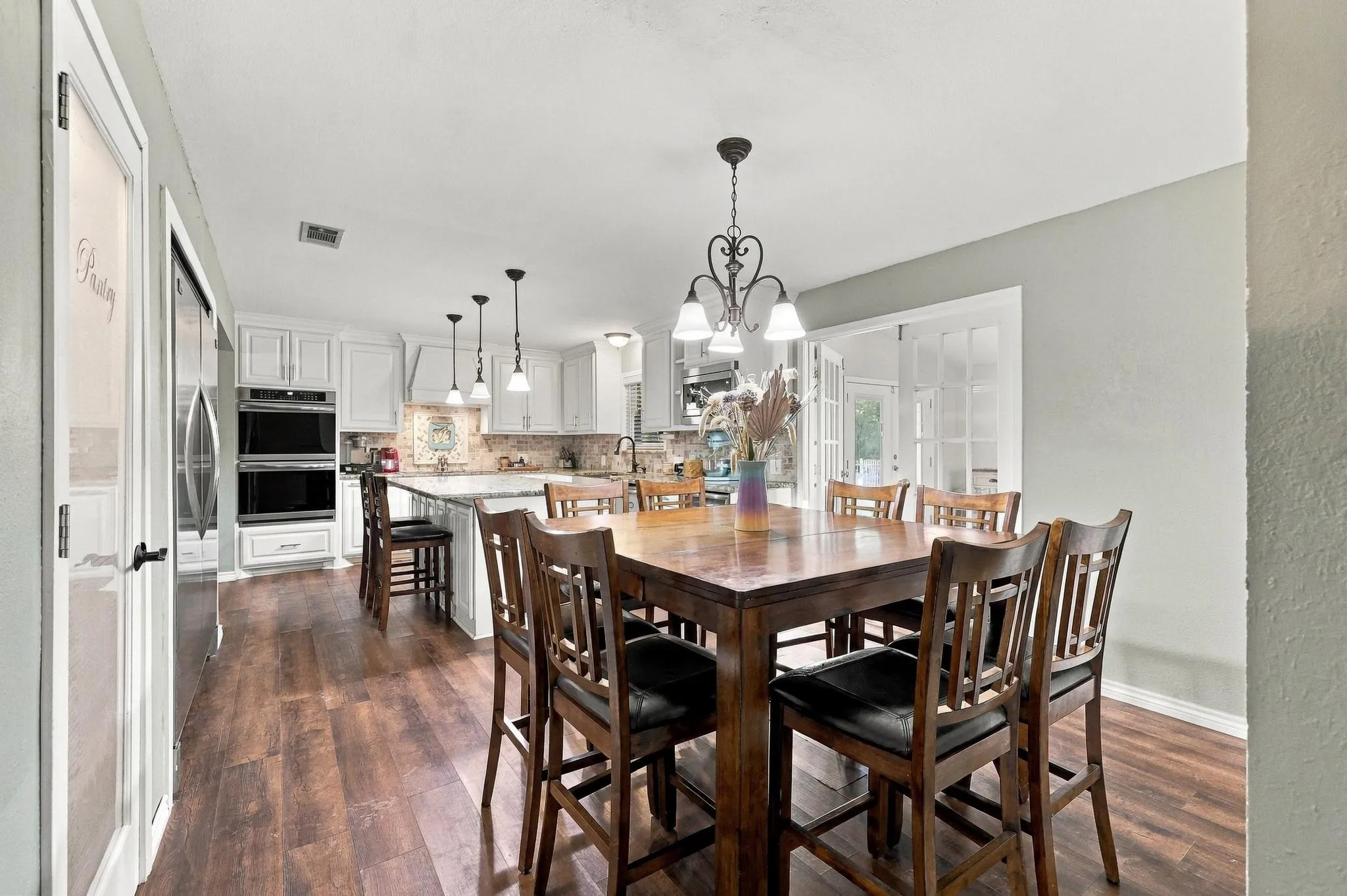 Kitchen featuring white cabinetry, stainless steel double wall ovens, a central island with bar seating, and wood-finish flooring