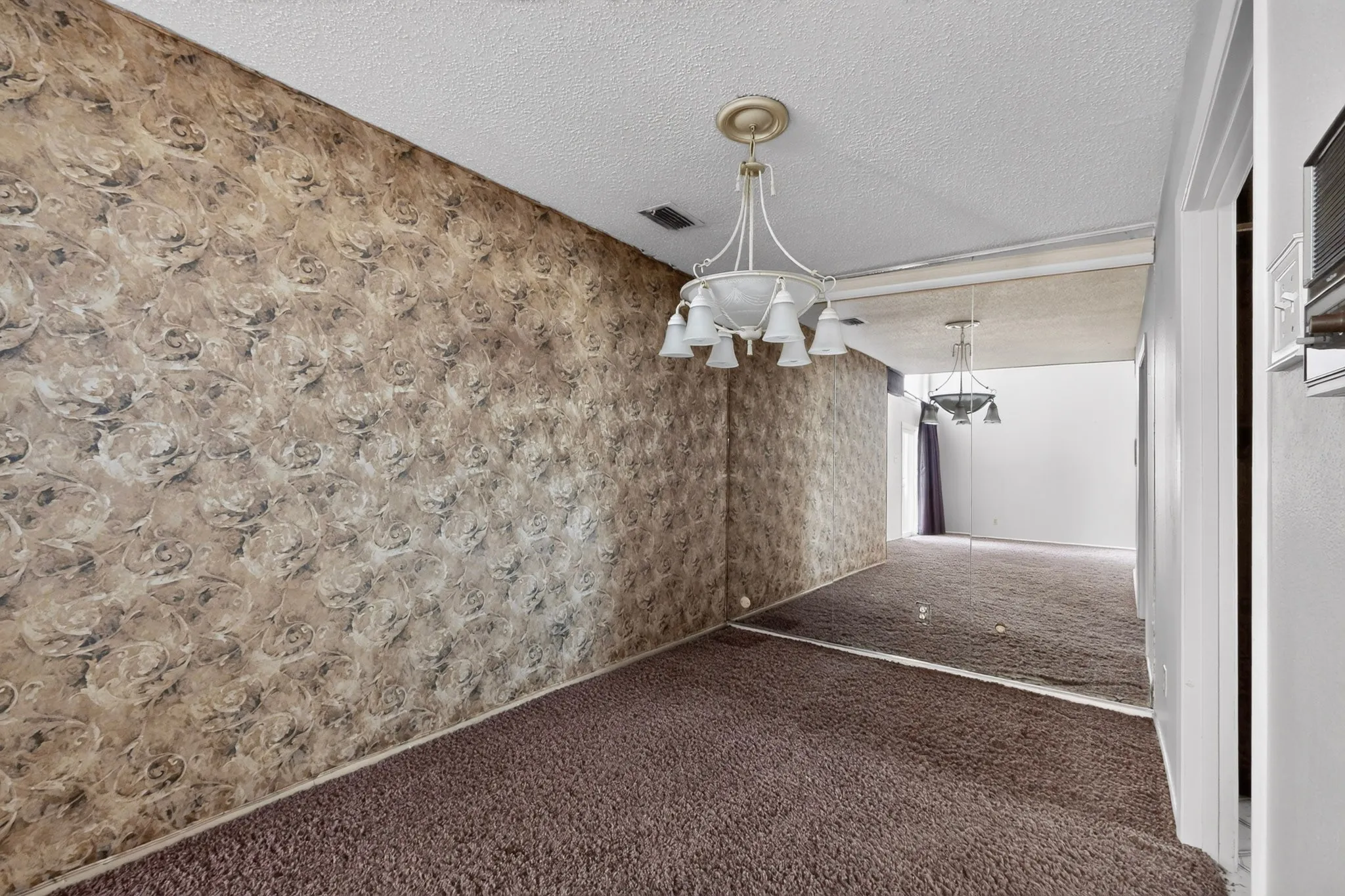 Wallpapered wall, carpeted flooring, mirrored wall, and overhead chandelier