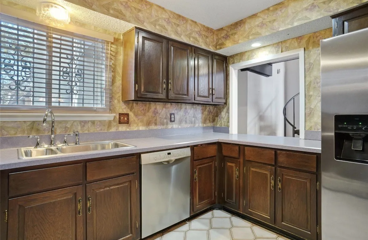 Kitchen featuring wood cabinetry, stainless steel dishwasher, stainless steel refrigerator, dual basin sink, and counter space