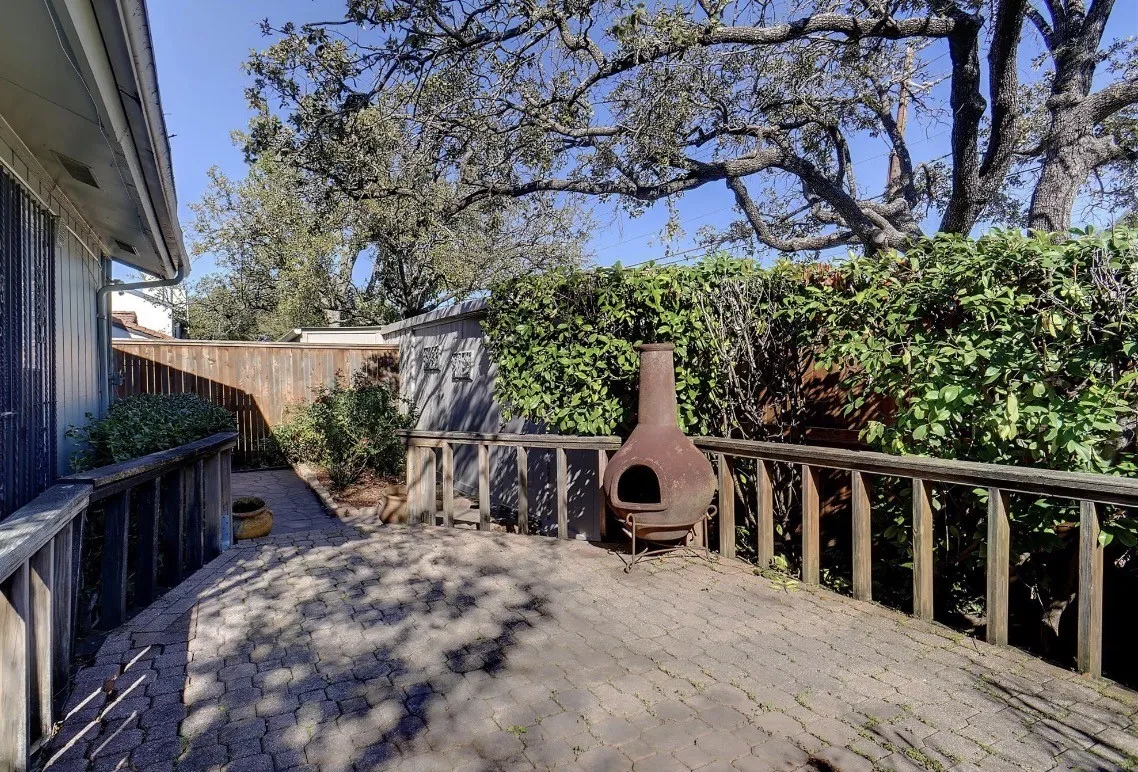 Paved patio surface, wood railing, privacy fencing, mature trees, and landscaping