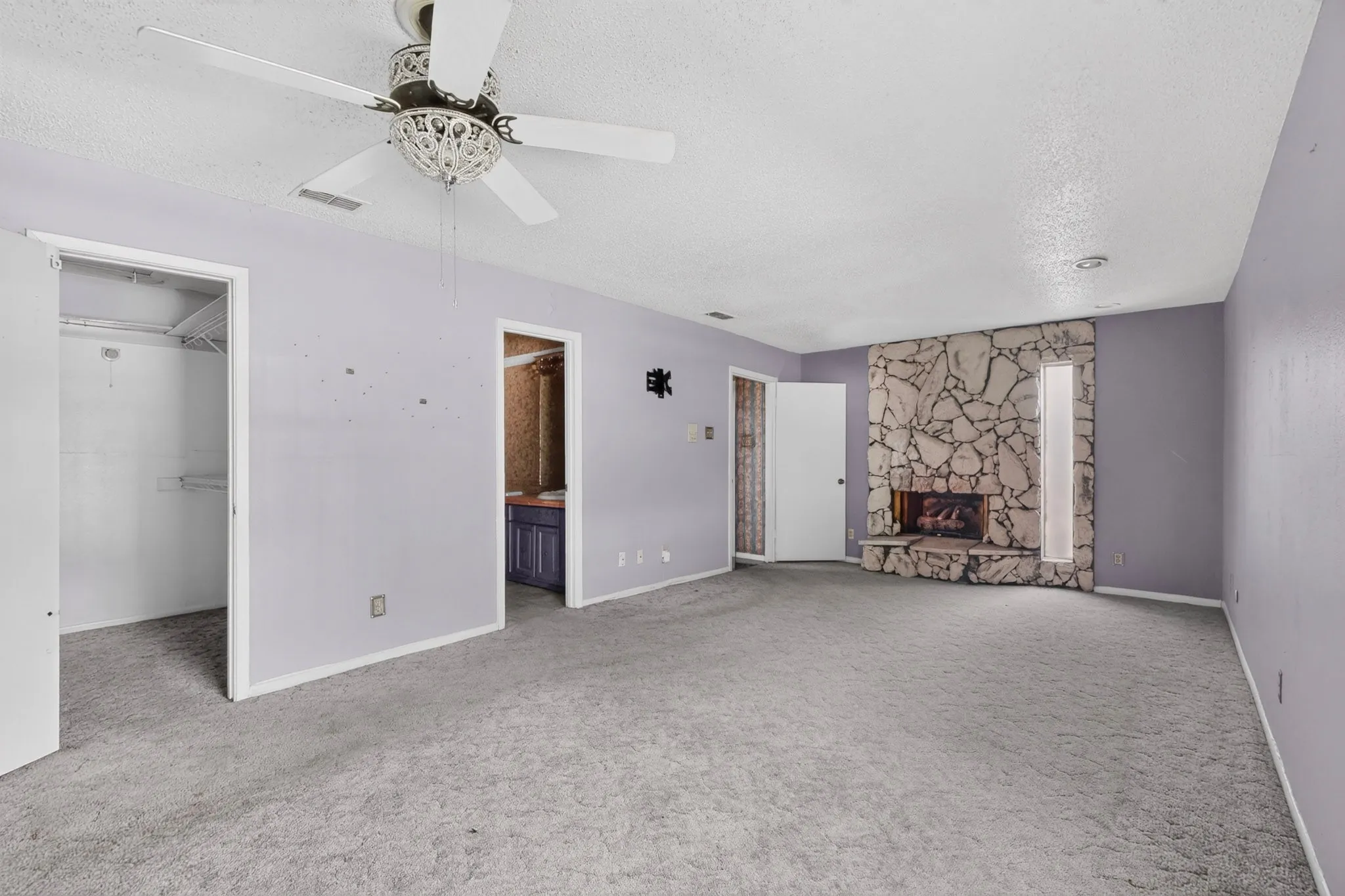 Stone-faced fireplace with a hearth, interior closet with shelving, and a ceiling fan with decorative light fixture