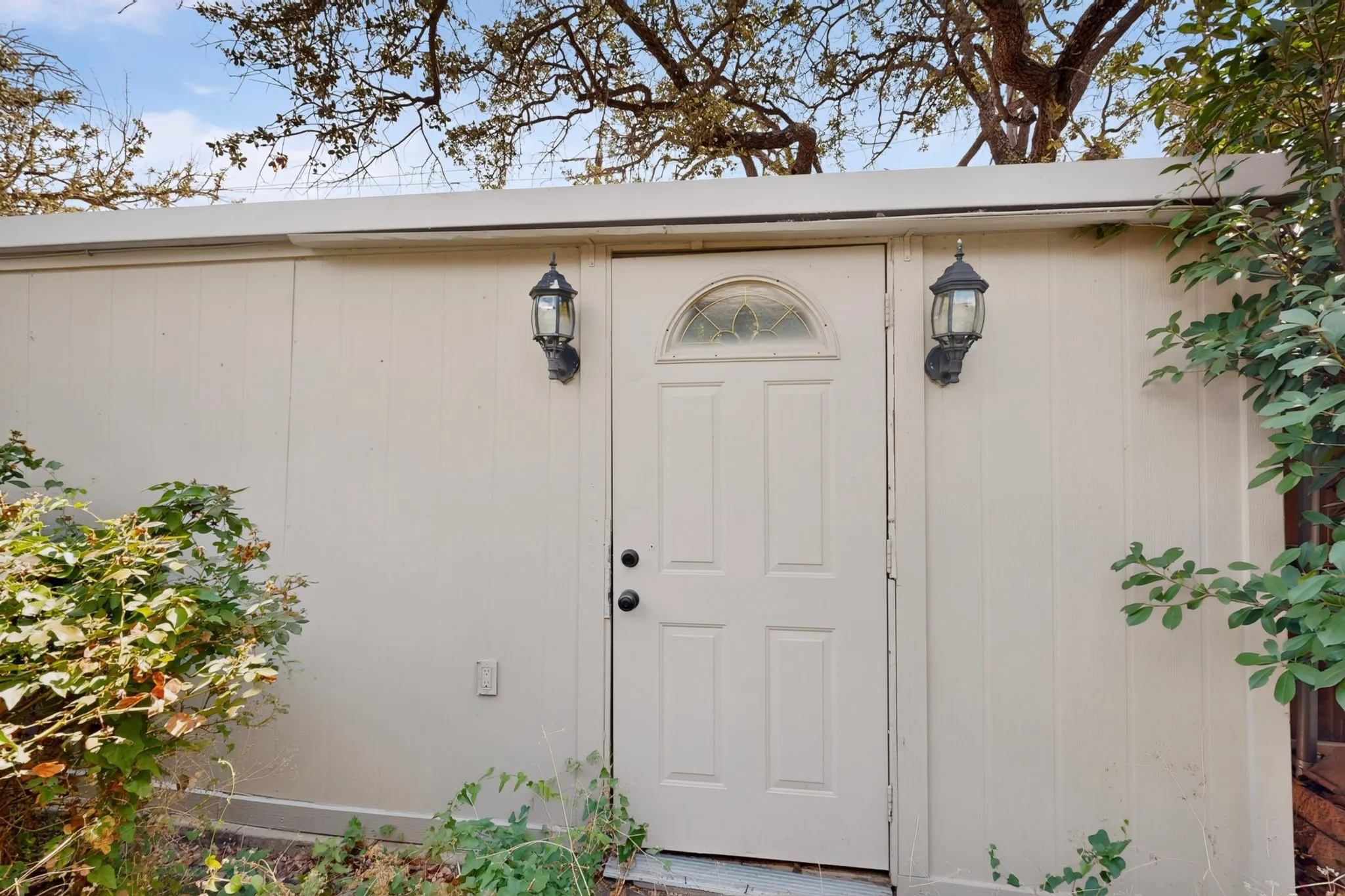 Exterior door to detached garage with an arched decorative glass insert and two outdoor sconce lights