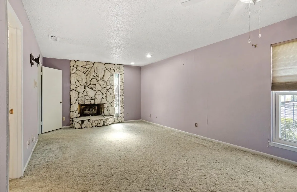 Stone-clad fireplace with hearth, recessed lighting, ceiling fan, and window with blinds