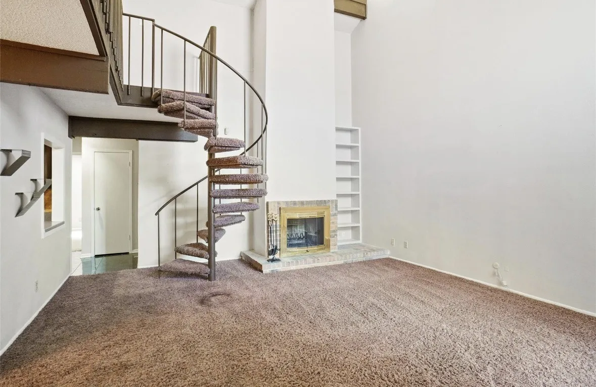 Spacious open floor plan featuring neutral carpet flooring, soaring two-story ceilings, and an architectural spiral staircase with metal railings